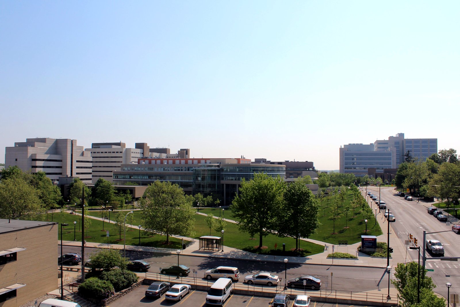 University of Michigan Medical Campus buildings rise beyond trees and a parking deck in Ann Arbor, photographed from an elevated street-level view.