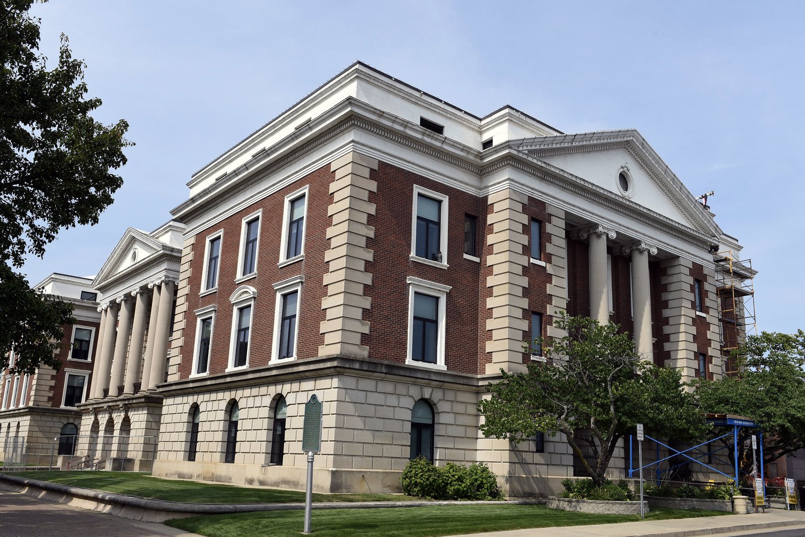 A large stone city hall building with tall arched windows and a central tower, seen from across a city street on a sunny day.