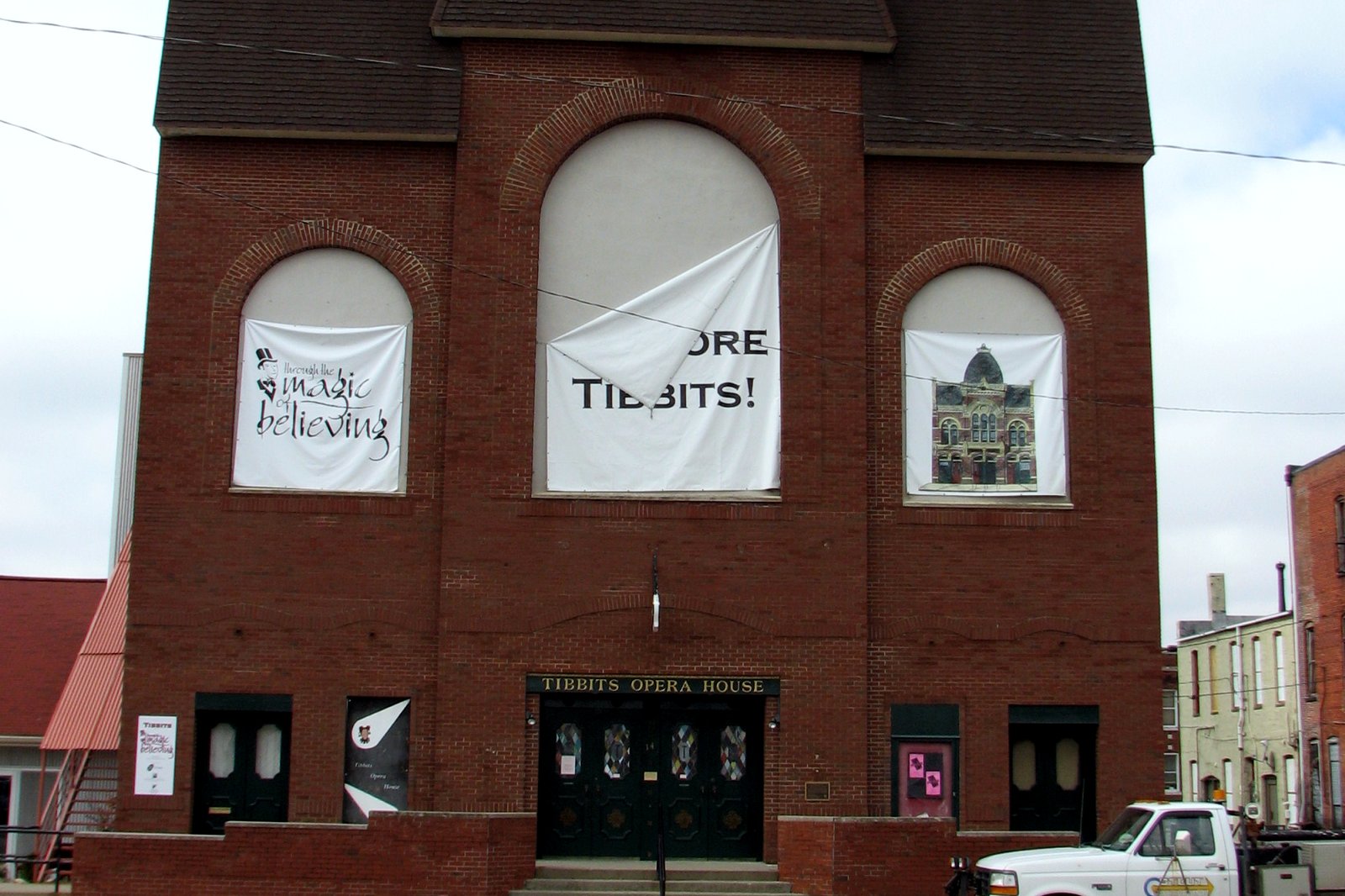 The red-brick front of Tibbits Opera House, with tall arched windows hung with banners and dark doors at street level beneath a Tibbits Opera House sign.