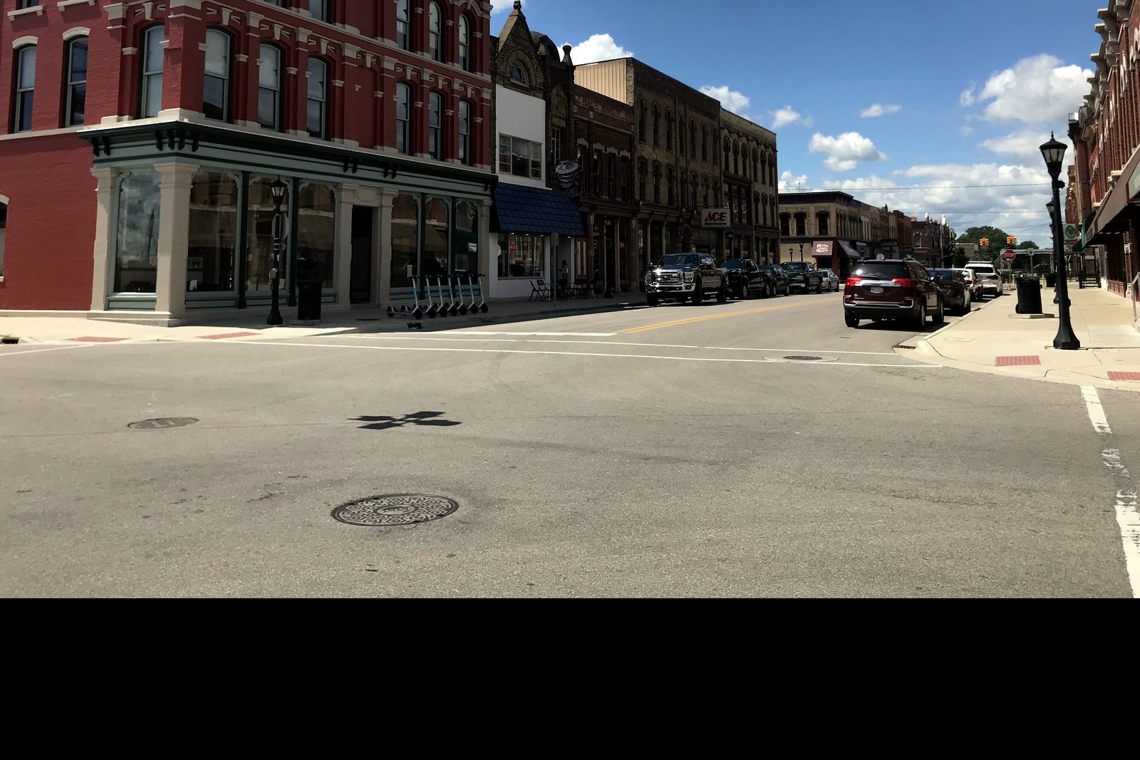A row of two- and three-story brick storefronts along Midland Street in Bay City under a blue sky, with parked cars along the curb.