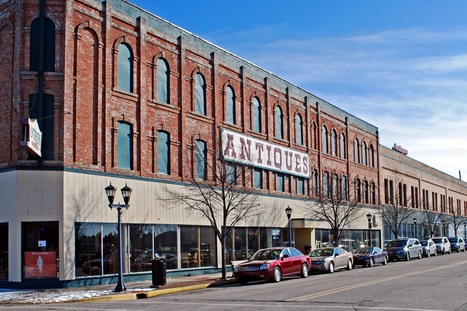 A long row of two- and three-story brick commercial buildings on a downtown street corner under a blue sky, with cars parked along the street.
