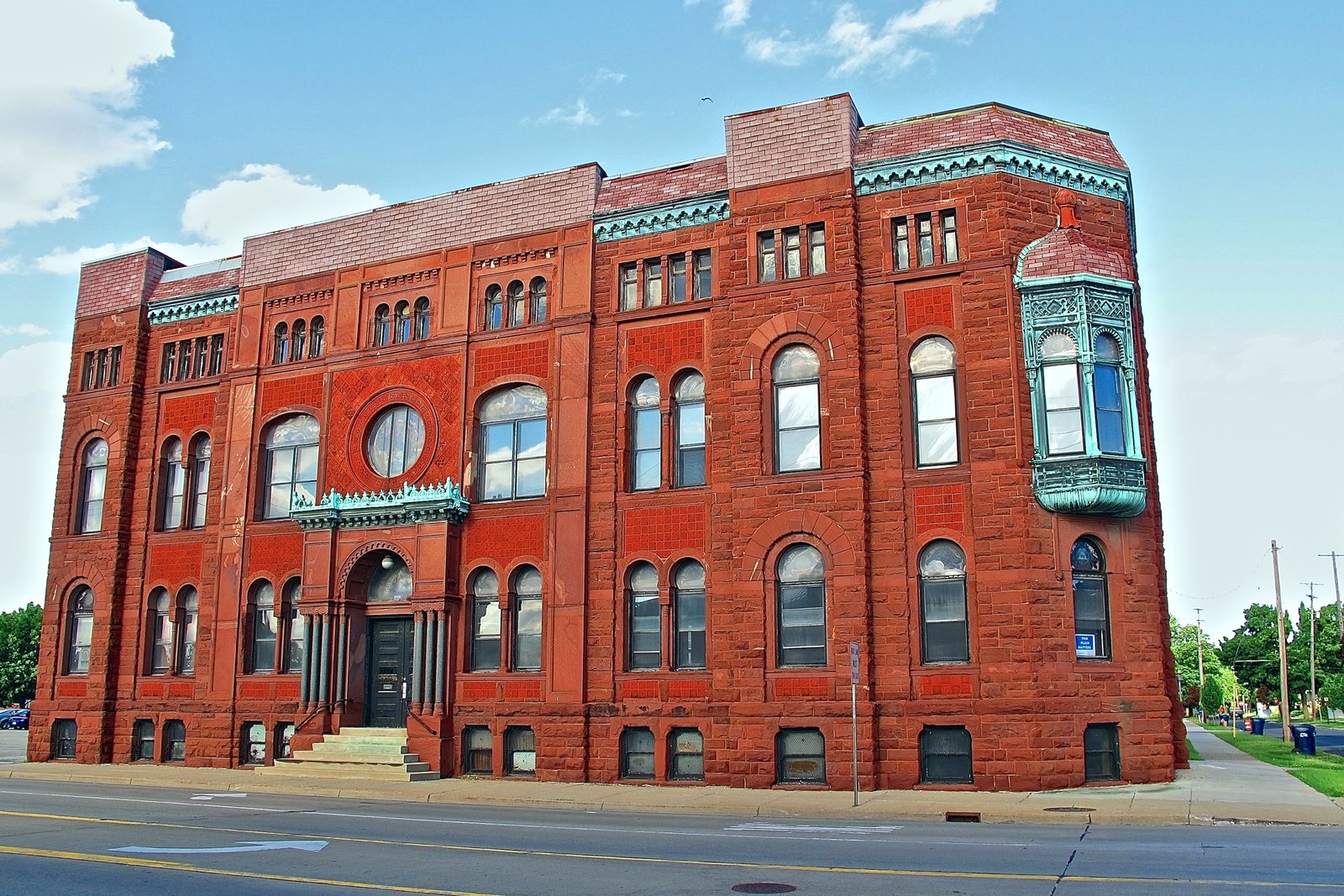 The red-brown sandstone facade of the Bay City Masonic Temple, with a raised arched entrance, stained-glass details and a corner bay, photographed from the street.