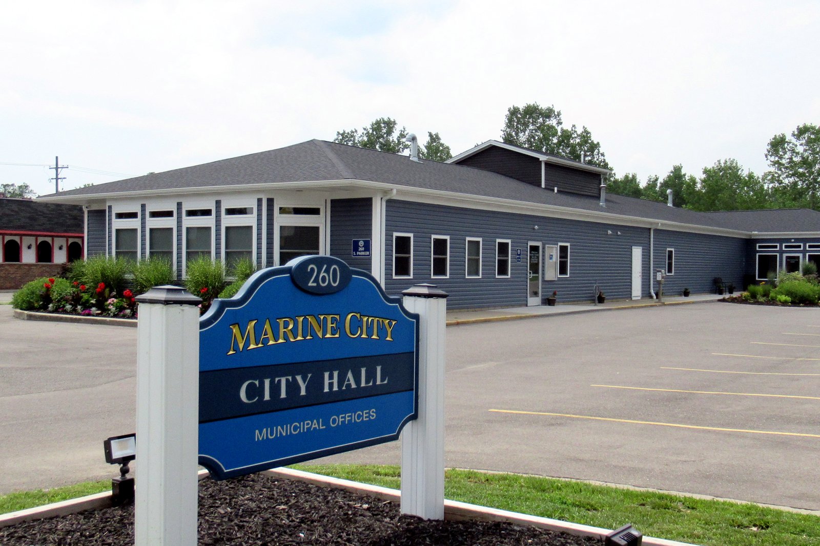 A blue sign reading 260 Marine City City Hall Municipal Offices in front of a gray single-story building with a parking lot.