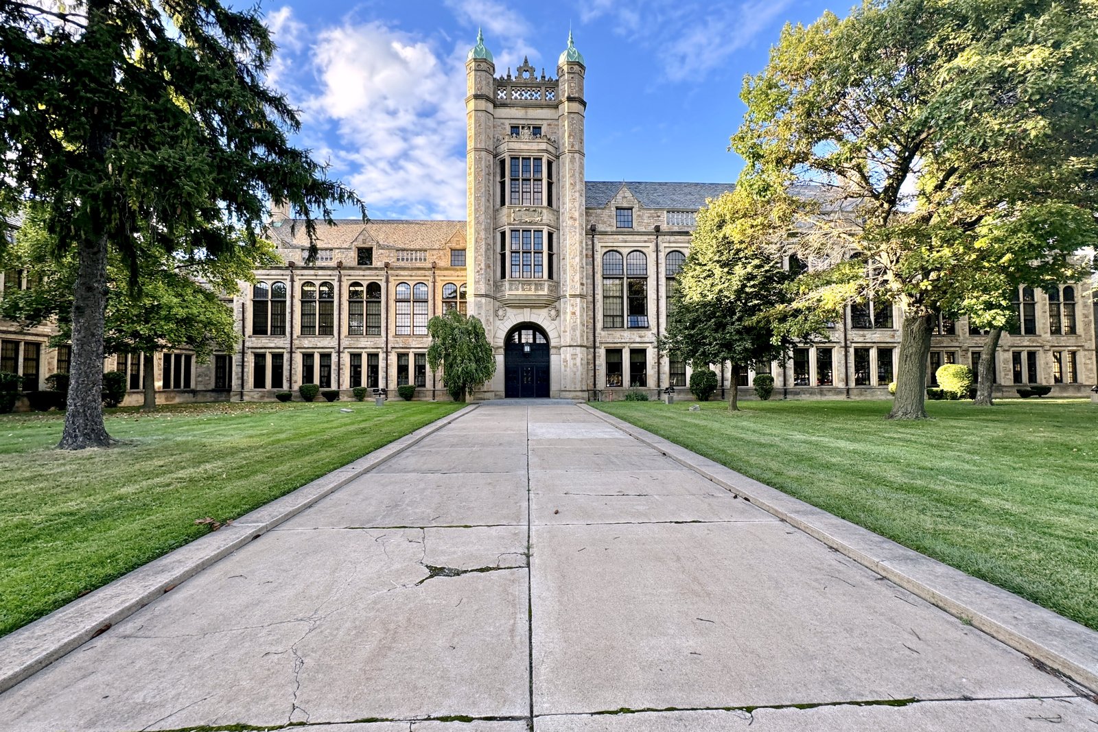A large brick Jacobethan Revival high school with a central tower, seen down a long walkway lined with lawns and trees.