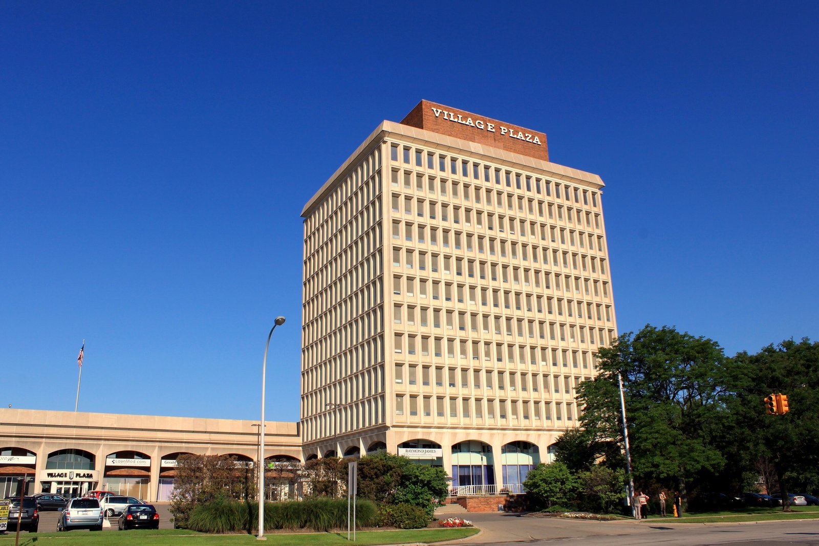 A tall white office tower with rows of windows behind low storefront buildings and a street, under a clear blue sky.