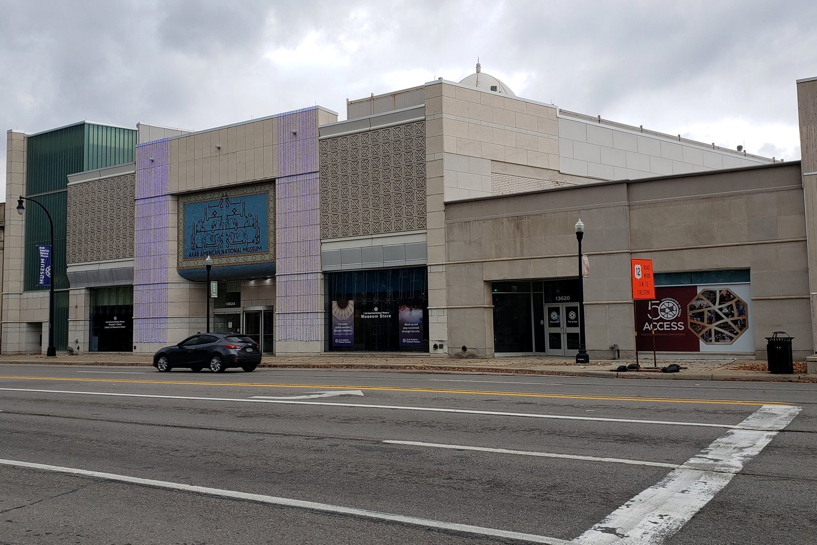 A modern tan stone and glass museum building on a city corner, with a crosswalk and street in the foreground.