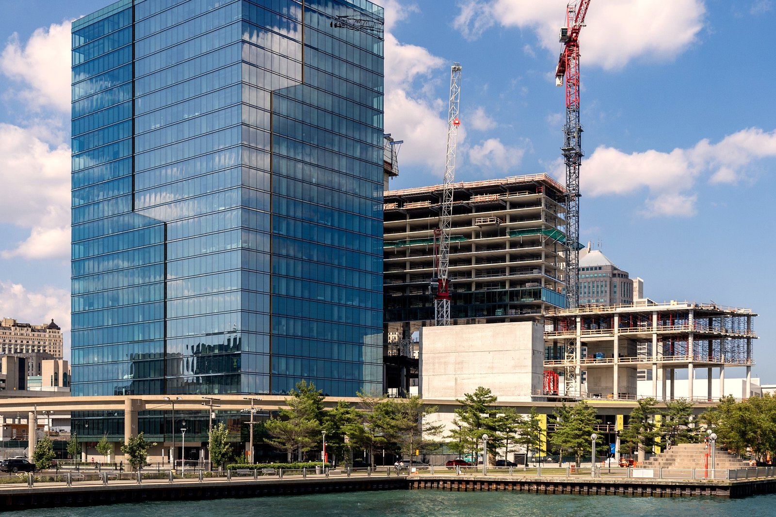 Tower cranes rise over a concrete apartment building under construction beside a finished glass high-rise along a river, in a file photo.