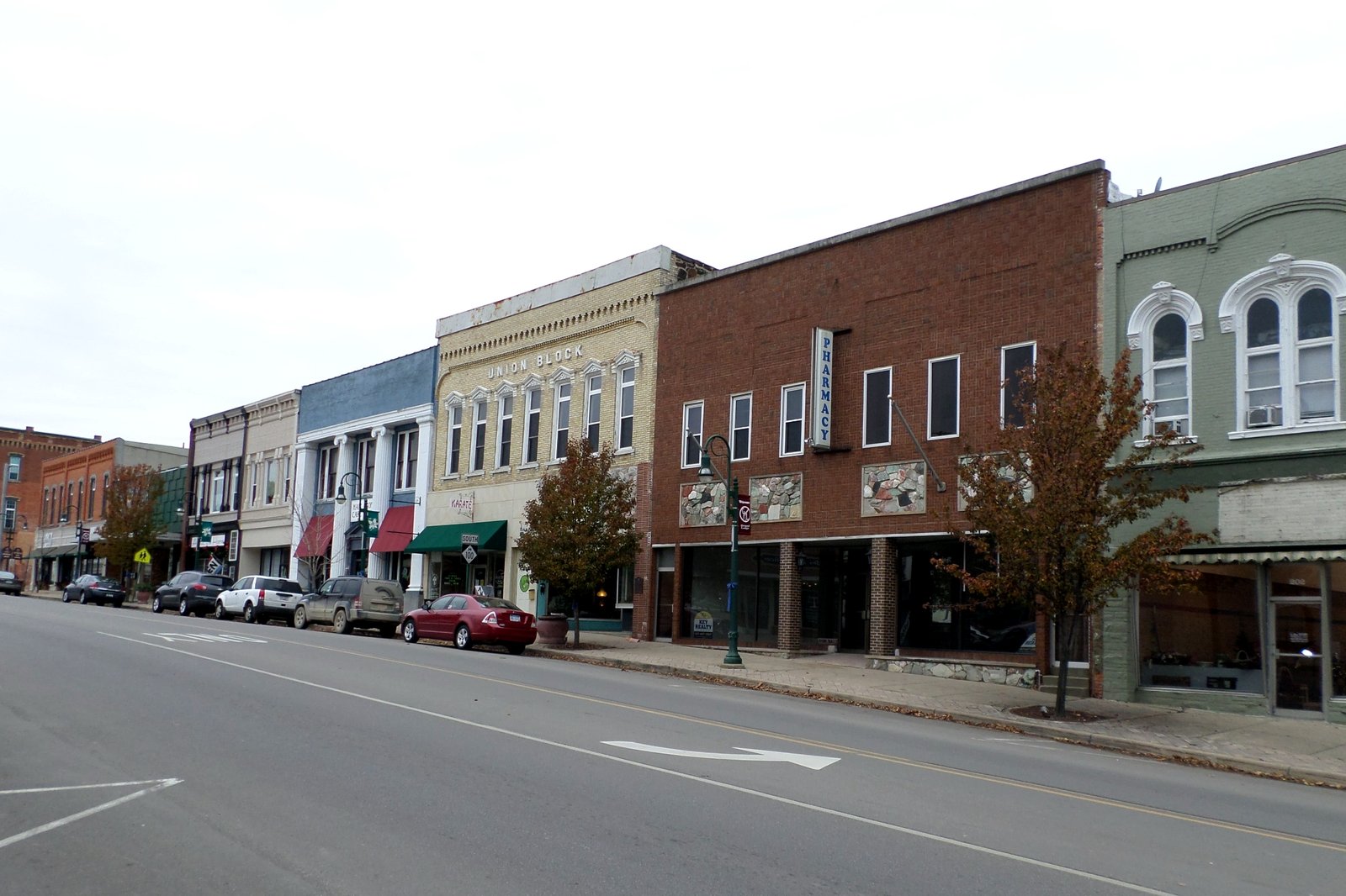 Two- and three-story brick and painted storefronts line a quiet downtown street under a gray sky.