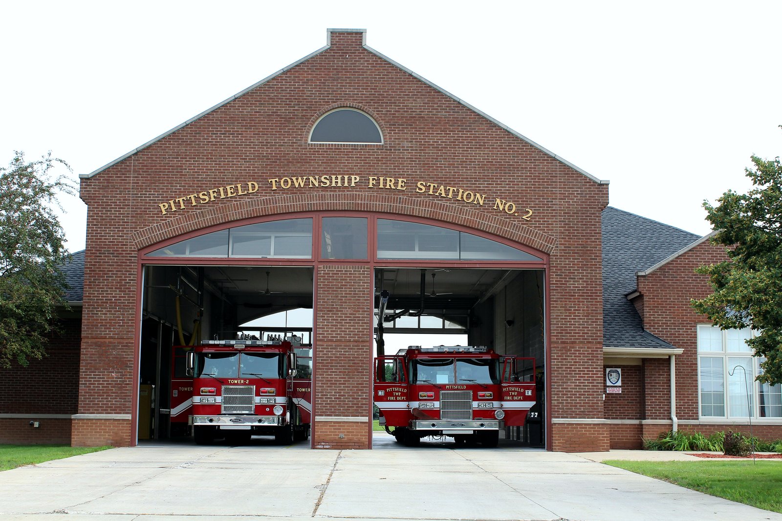 A red brick fire station with an arched front and the words Pittsfield Township Fire Station No. 2 above two open bay doors, with two red fire trucks parked inside.