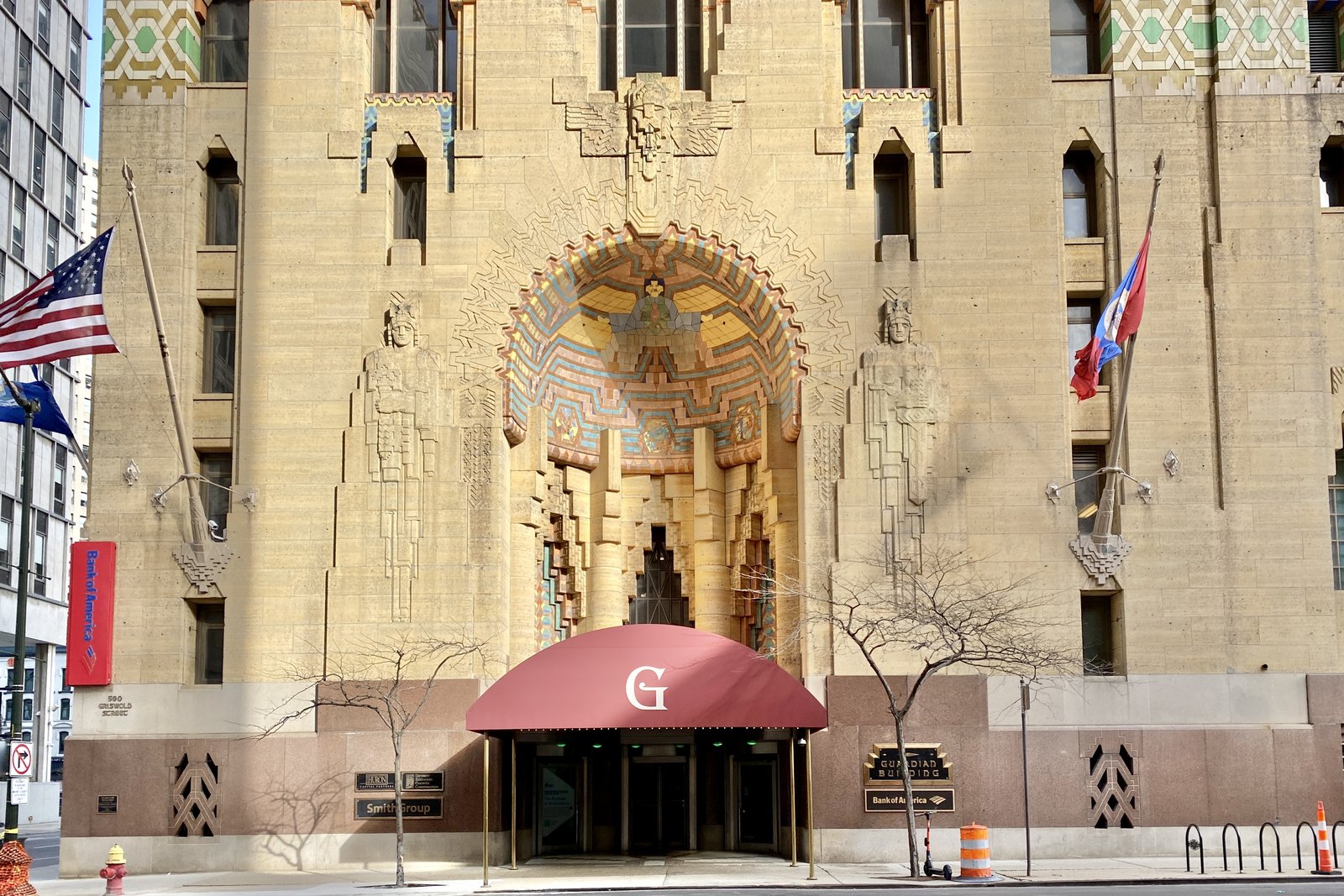 The Art Deco entrance of the Guardian Building in downtown Detroit, a tiled arch above a maroon awning marked with a G, flanked by flags.