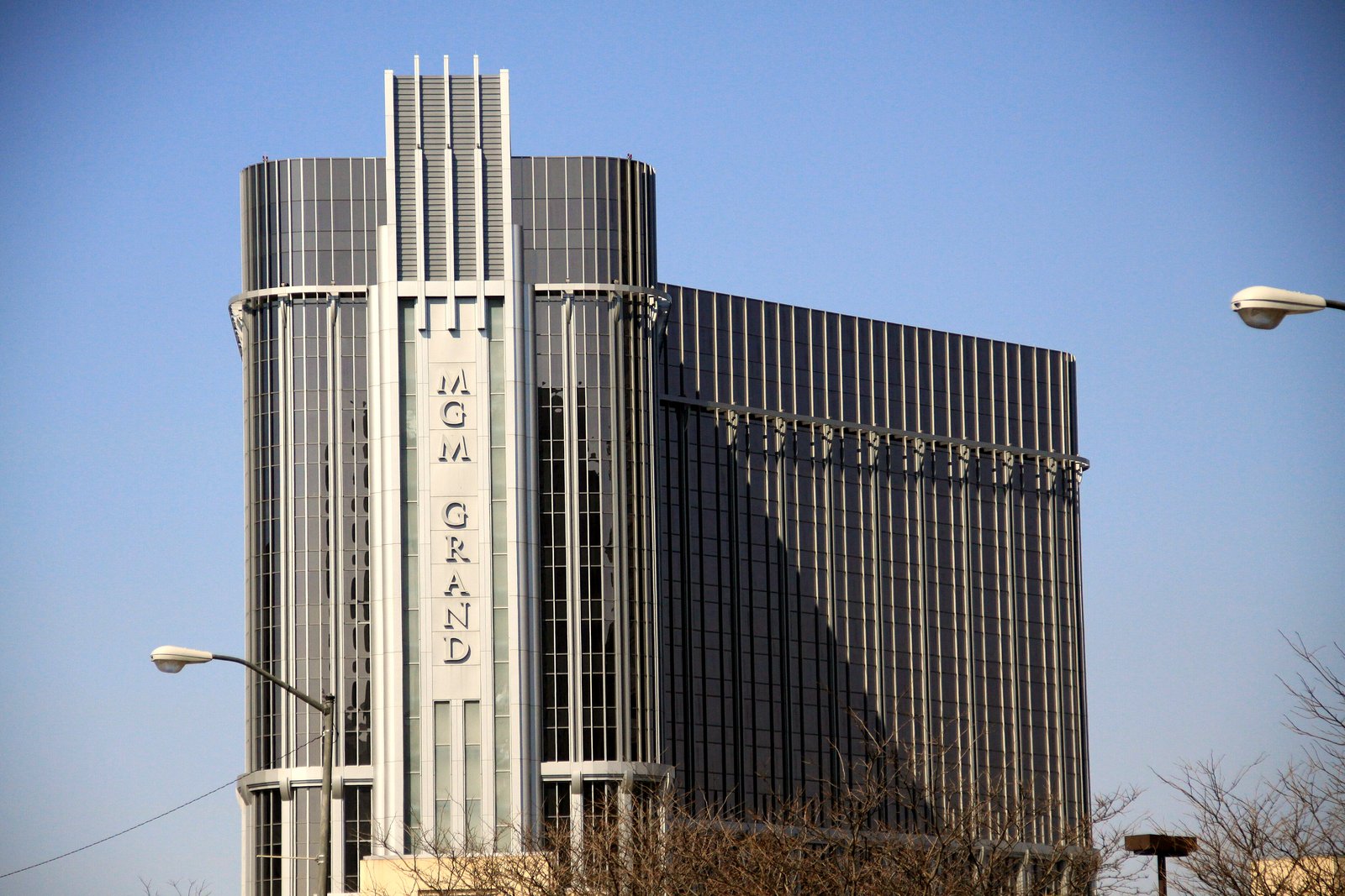 The silver MGM Grand tower in Detroit with its vertical name sign against a clear blue sky.