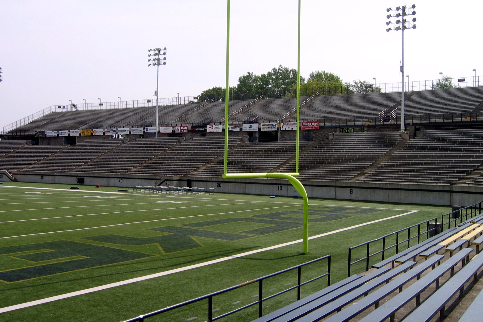 An empty football stadium with a yellow goalpost, green artificial turf and rows of gray bleachers under a pale sky, in a file photo.