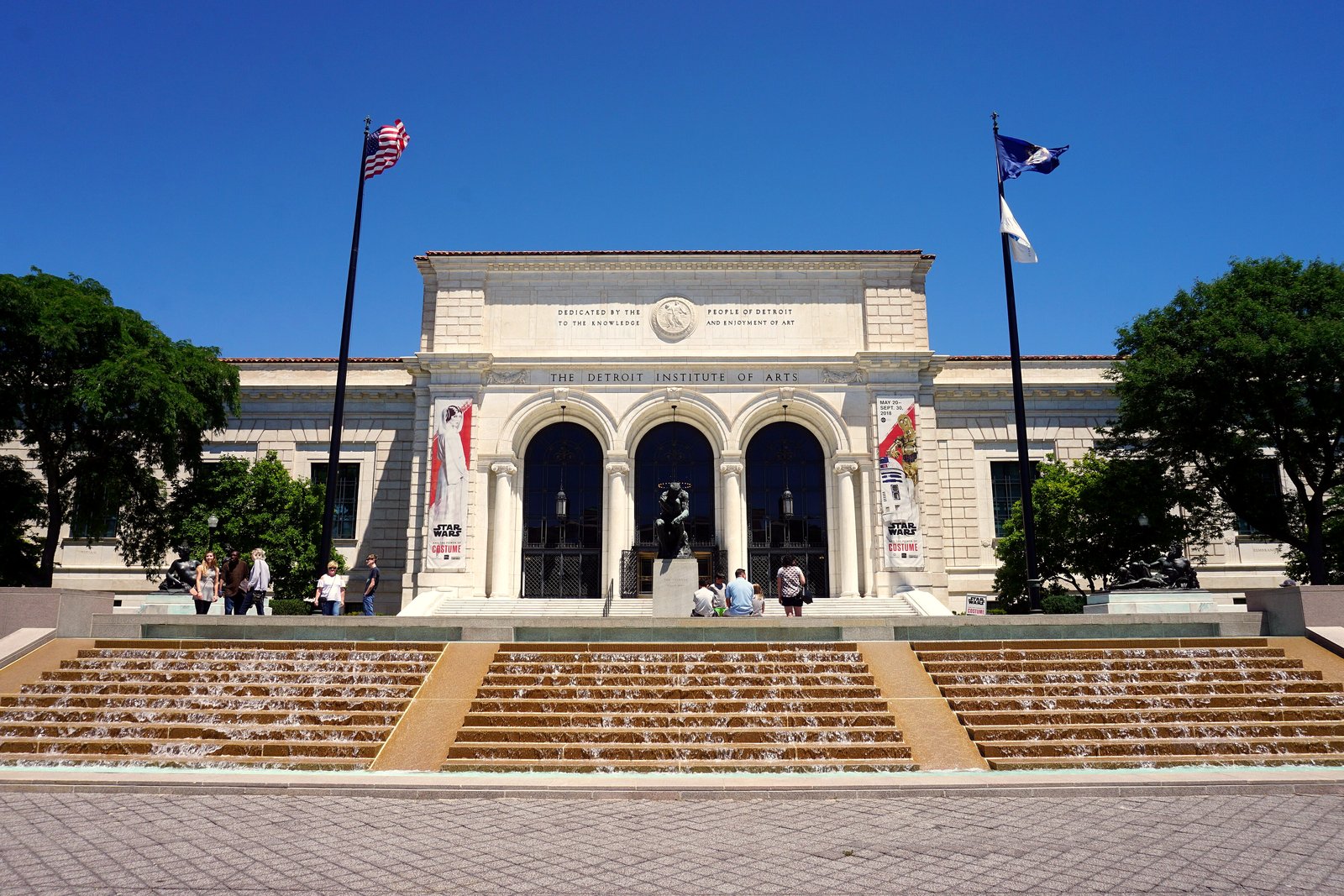 The white marble front of the Detroit Institute of Arts, with arched entrances, flags and wide front steps.