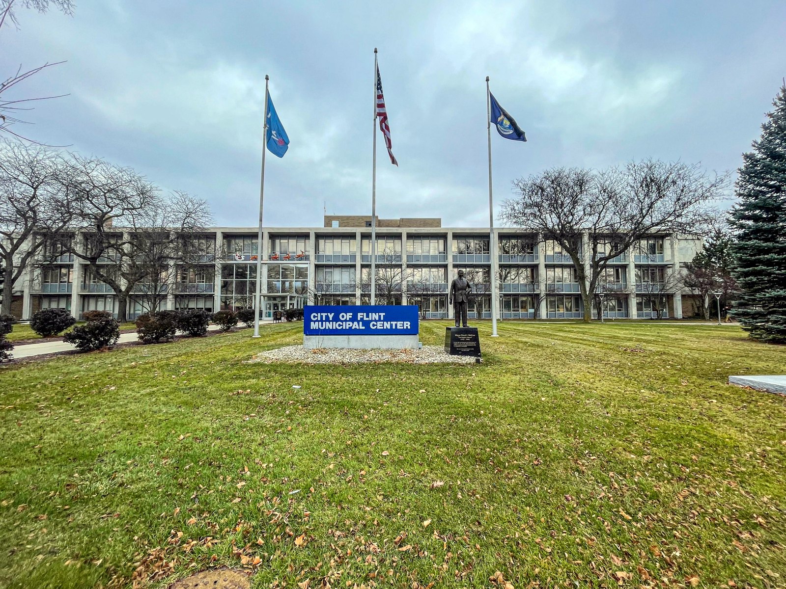 The City of Flint Municipal Center, a long low office building behind a lawn with three flagpoles and a blue City of Flint Municipal Center sign.