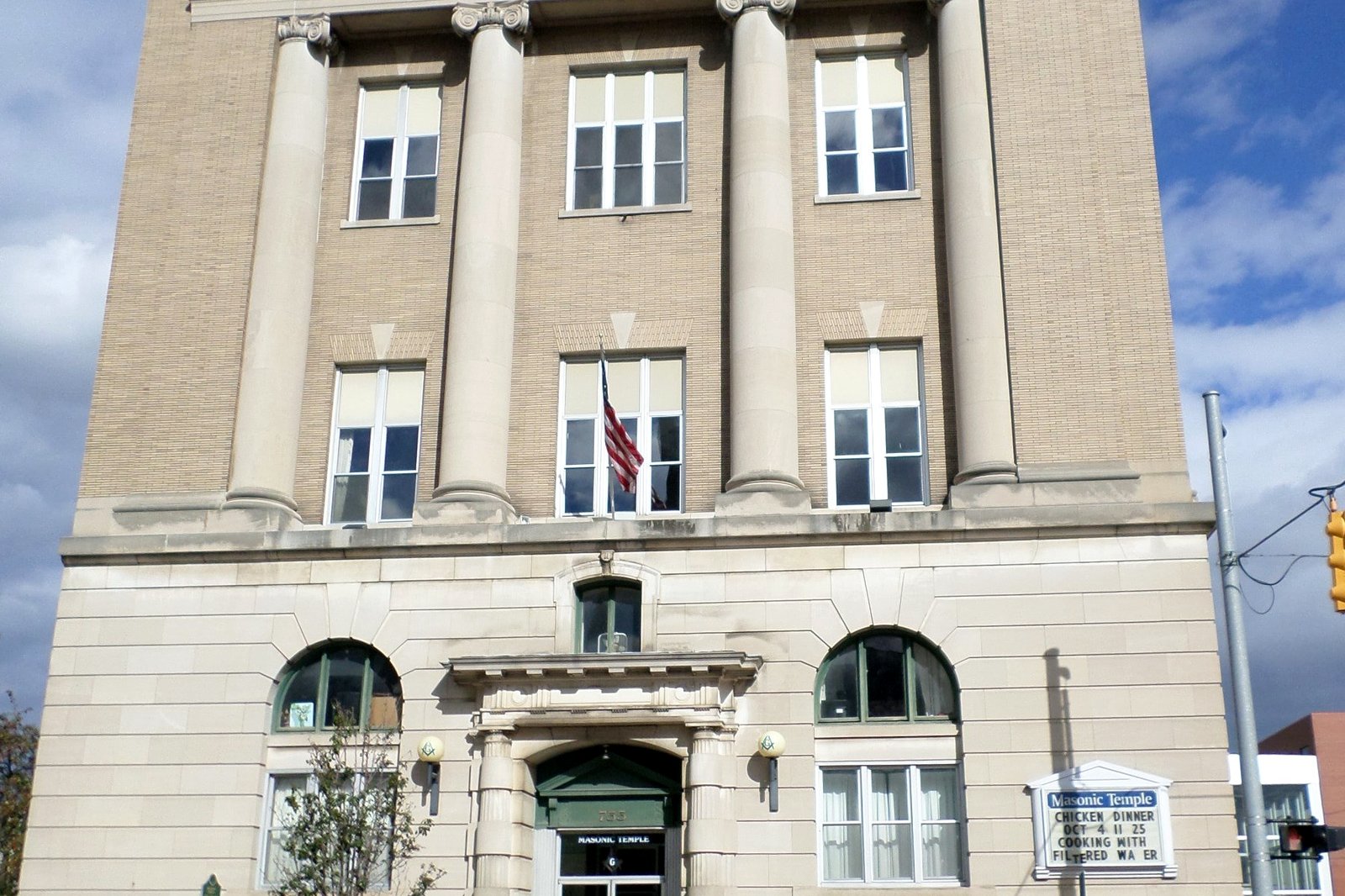 The pale stone front of the Flint Masonic Temple on Saginaw Street, with tall columns, rows of windows and an American flag over the arched entrance.