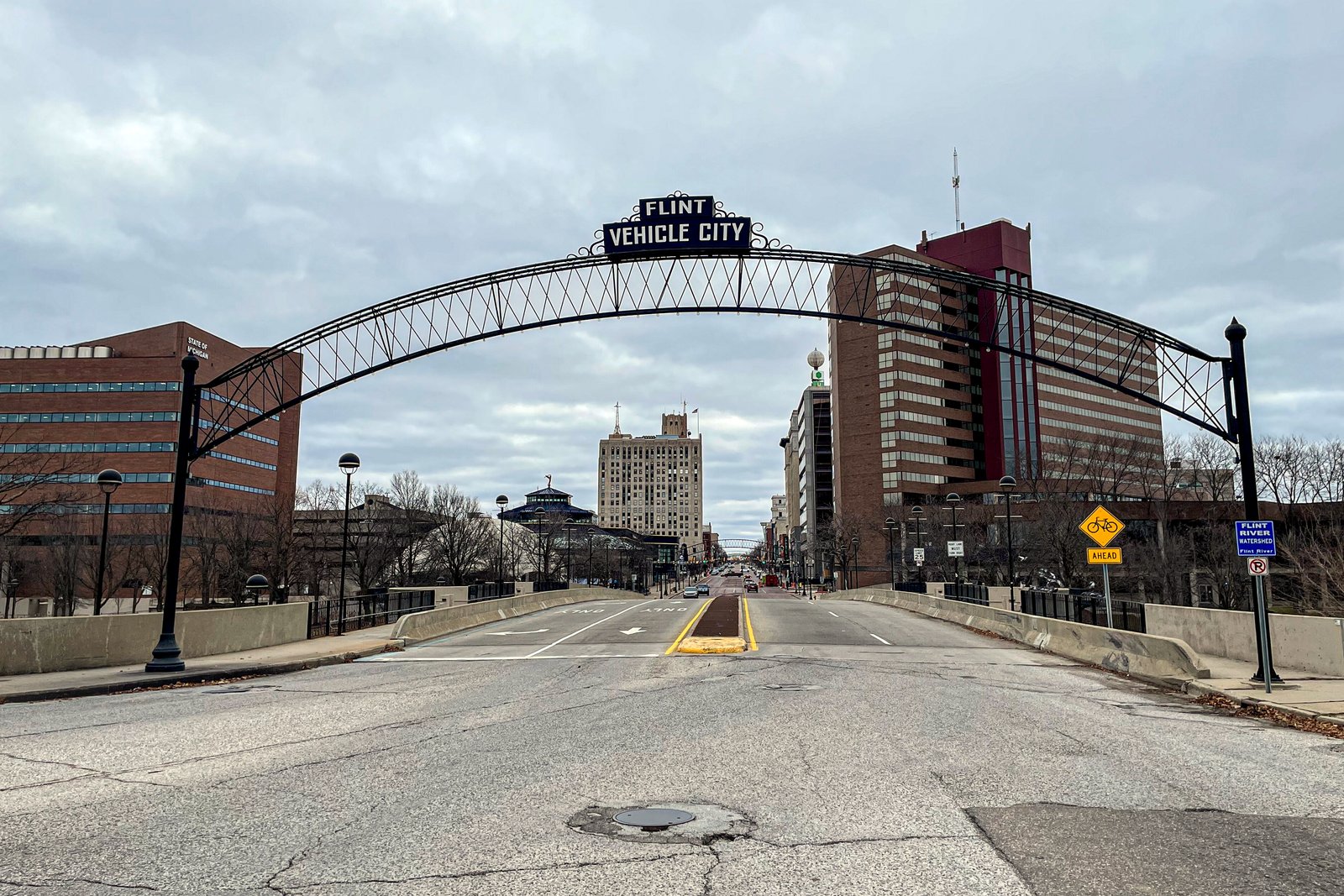 A steel arch lit with the words Vehicle City spans a wide downtown street lined with brick buildings under a cloudy sky.