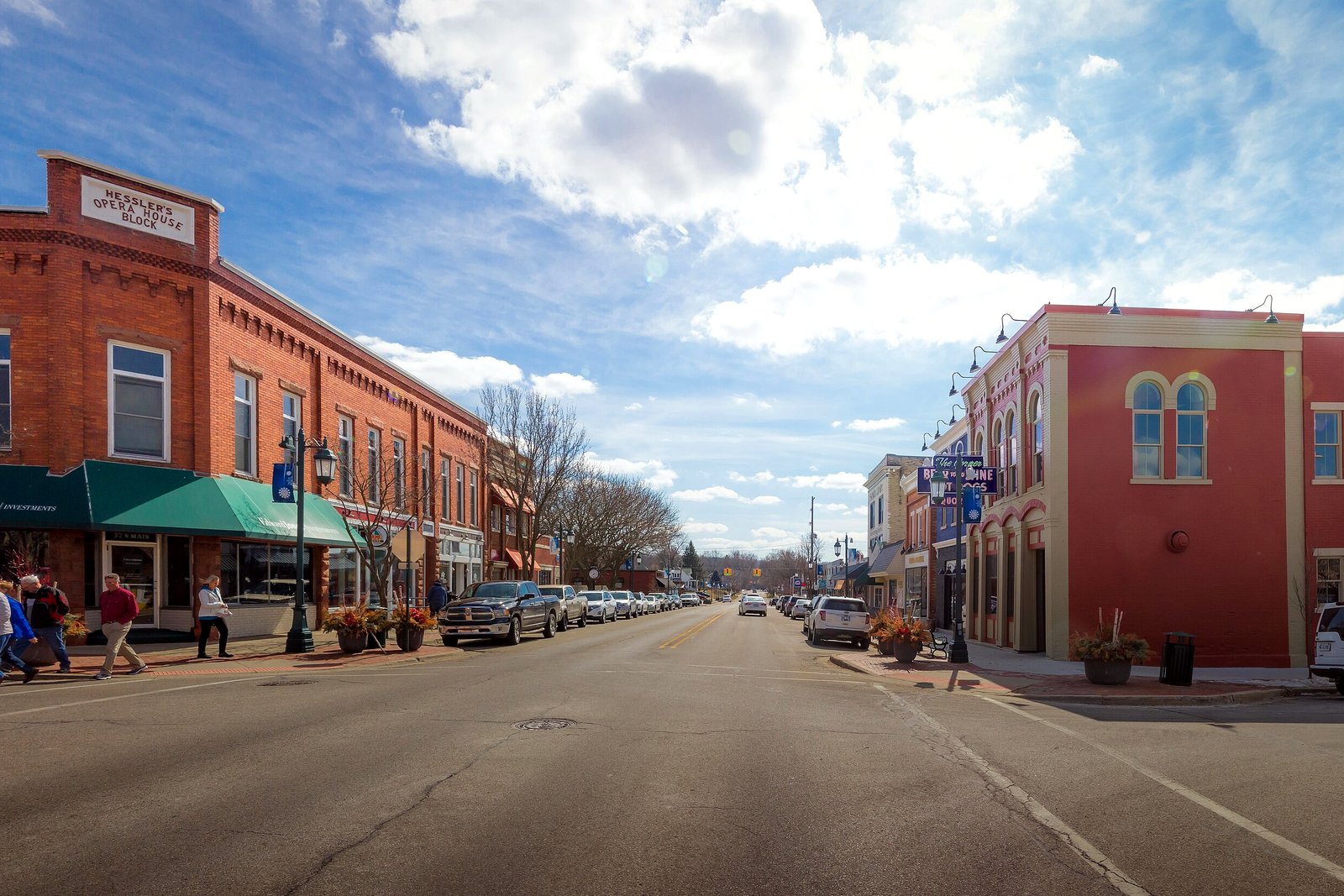 A wide main street lined with two- and three-story brick storefronts under a partly cloudy blue sky.