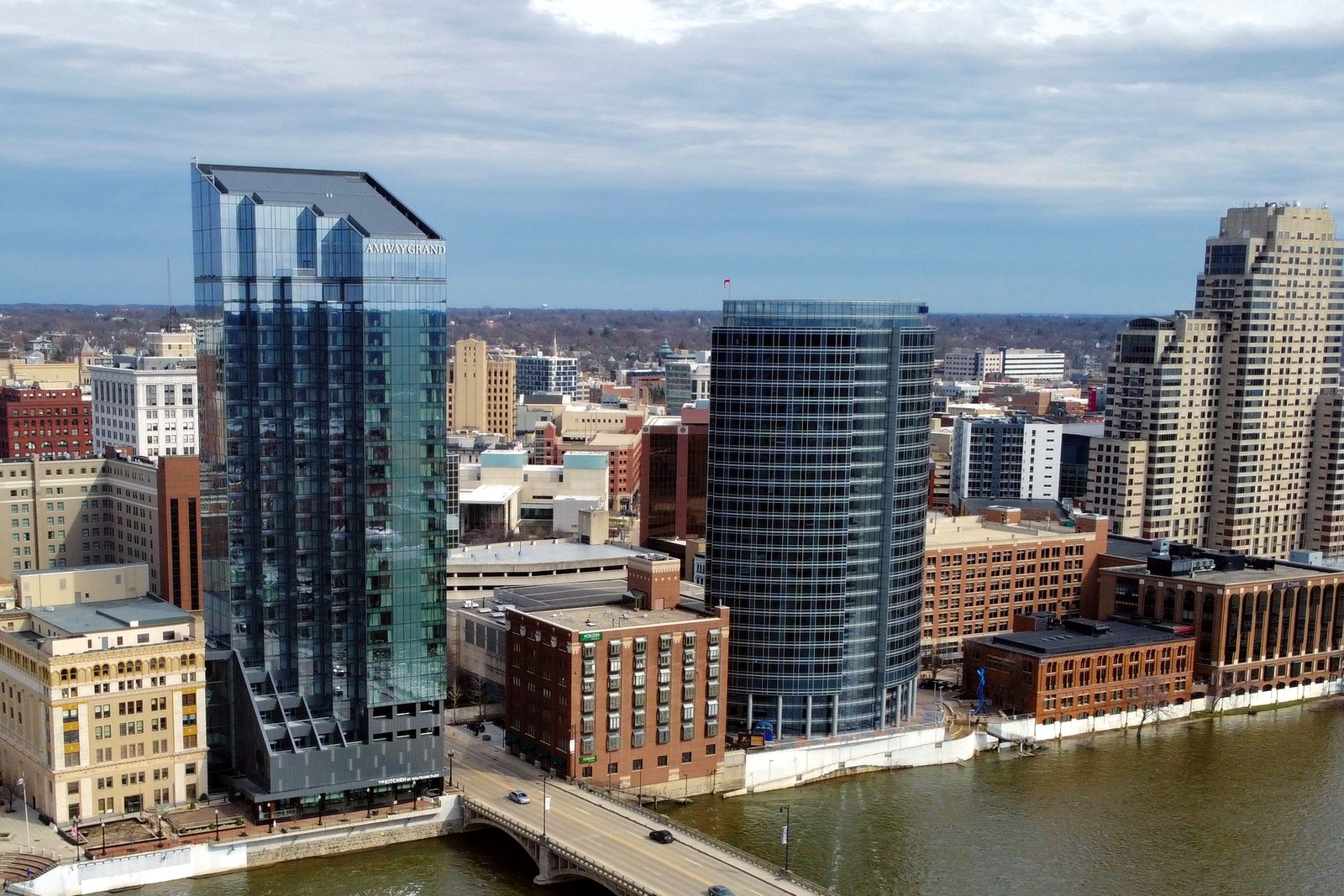 Downtown Grand Rapids high-rise towers and brick buildings beside the Grand River and a bridge, seen from above on a clear day.