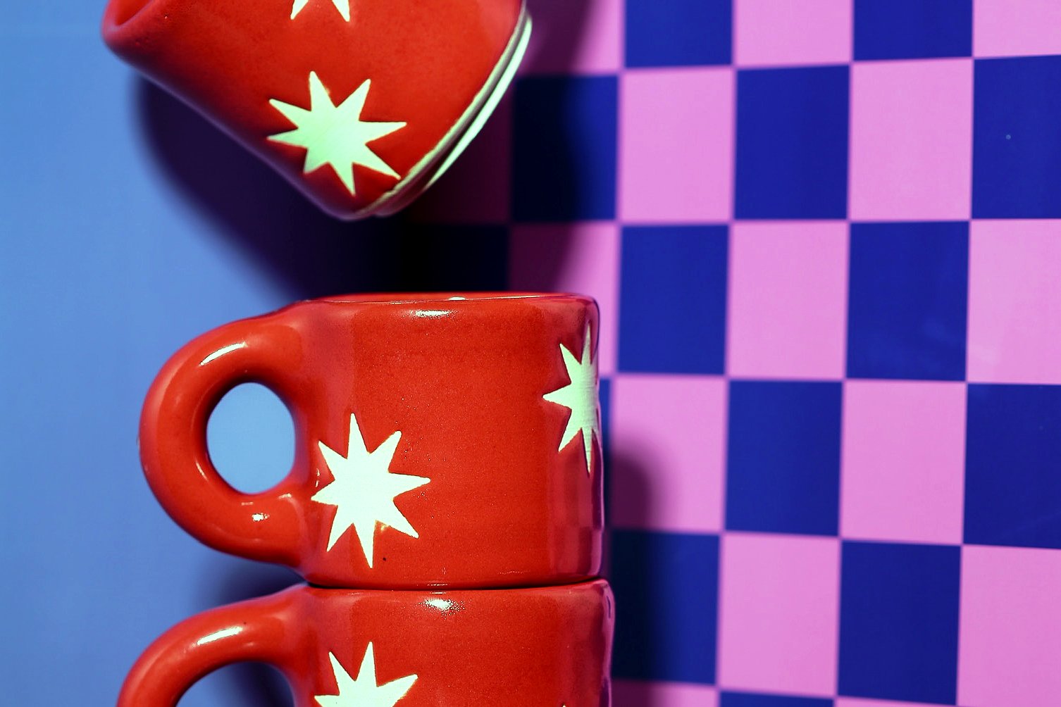 Red mugs with white star designs stacked in a column against a purple and pink checkered background.