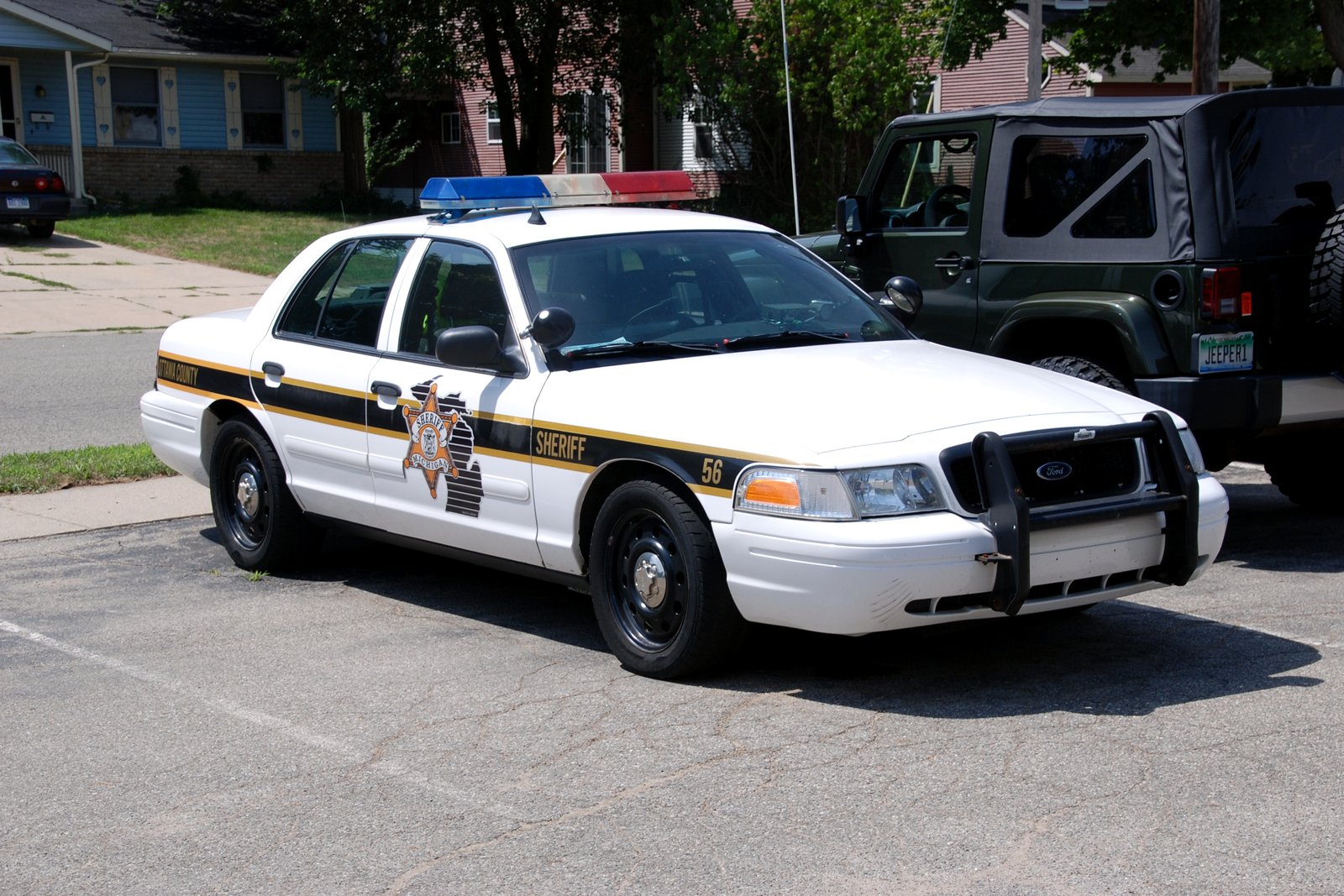 A white Ottawa County Sheriff patrol car with a light bar parked on a residential street.