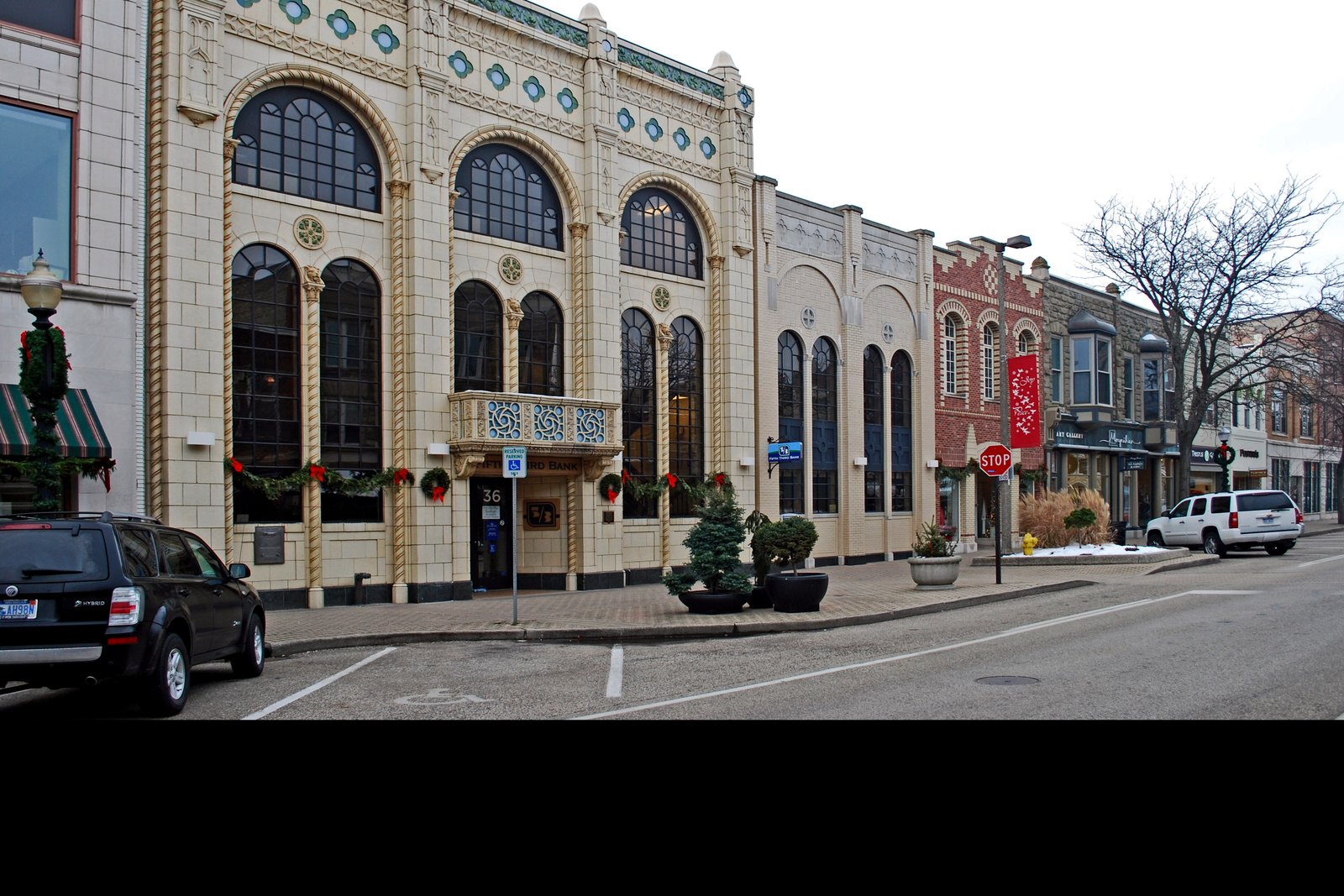 A row of historic downtown storefronts, led by a cream-colored terra-cotta building with tall arched windows trimmed with holiday wreaths and garland, on a gray winter day.