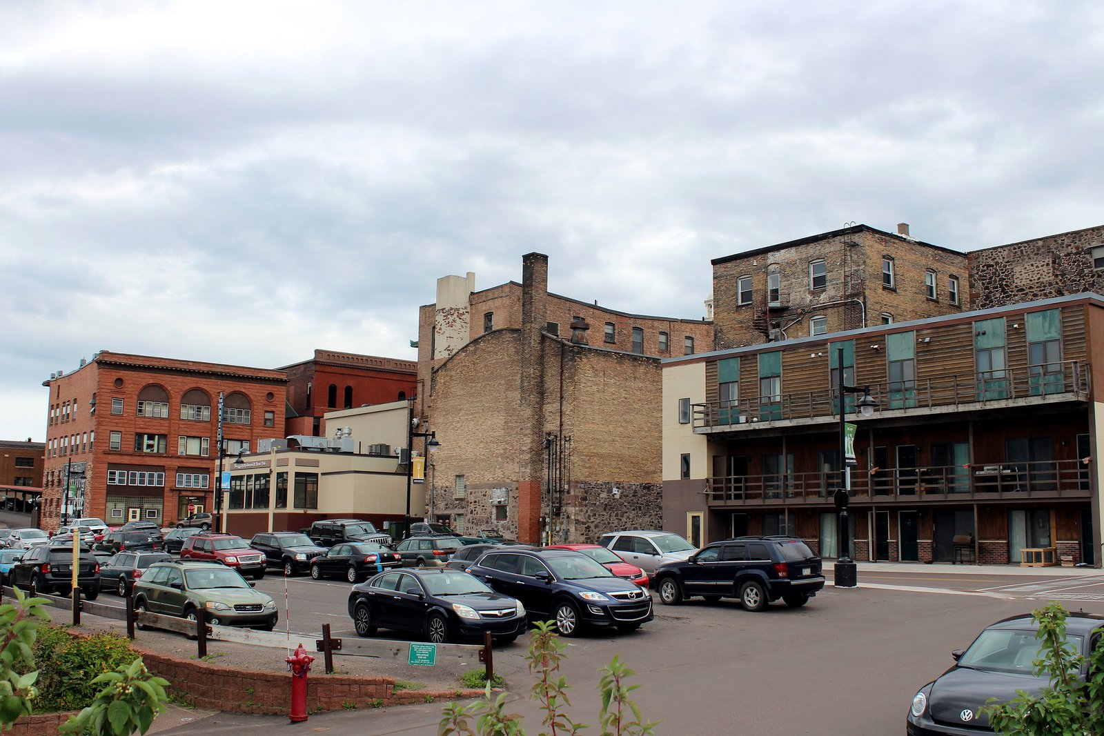 Brick commercial buildings rise behind a parked-car lot in downtown Houghton.