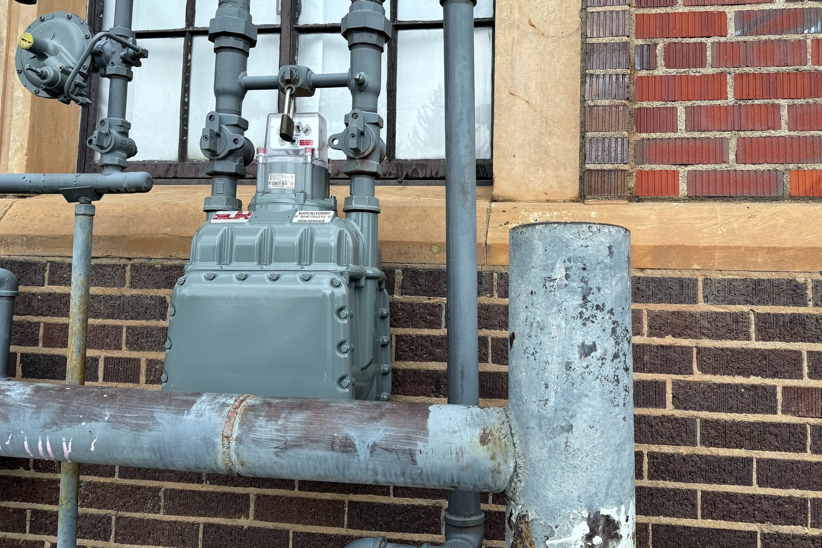 A gray natural gas meter and pipes mounted against a brick wall.