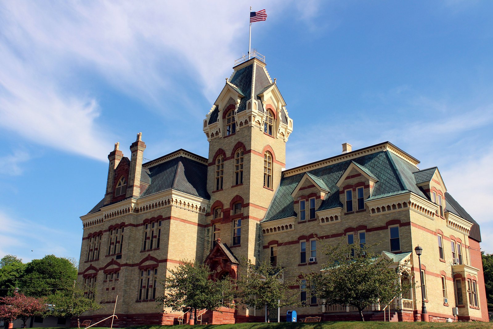 The red sandstone Houghton County Courthouse in Houghton, Michigan, with its tall clock tower and green roof, under a blue sky.