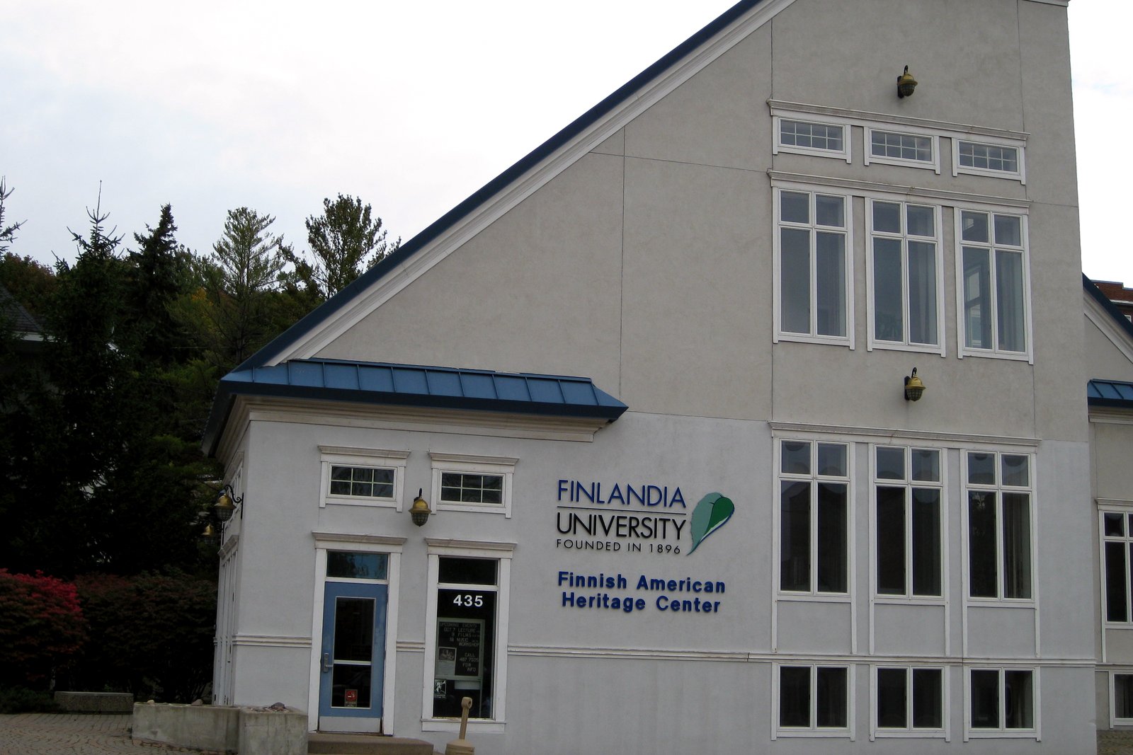 A two-story white and gray building with a sign reading Finnish American Heritage Center, on a summer day.