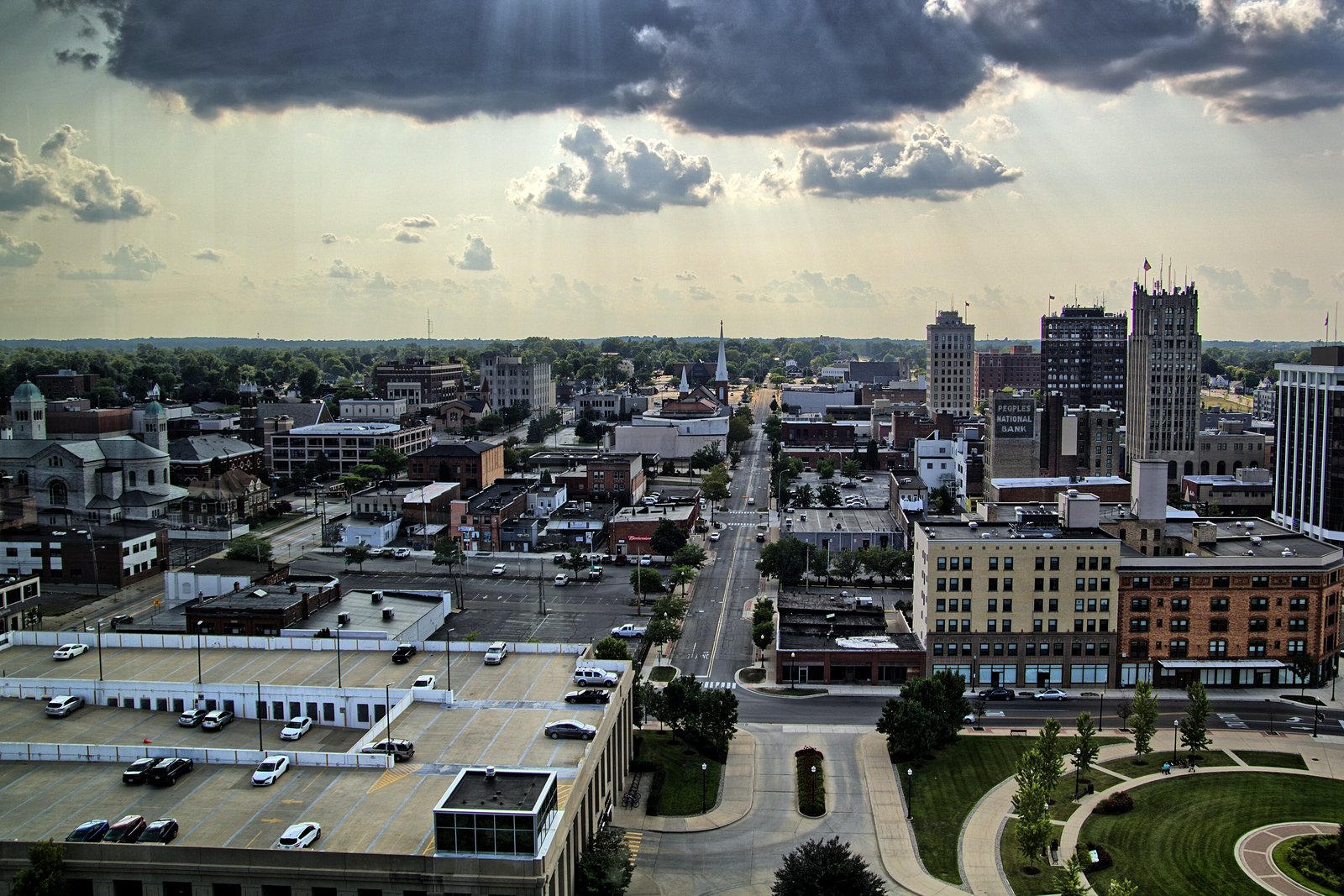 An elevated view of downtown Jackson, Michigan, with brick buildings, a parking deck and streets under a cloudy late-day sky.