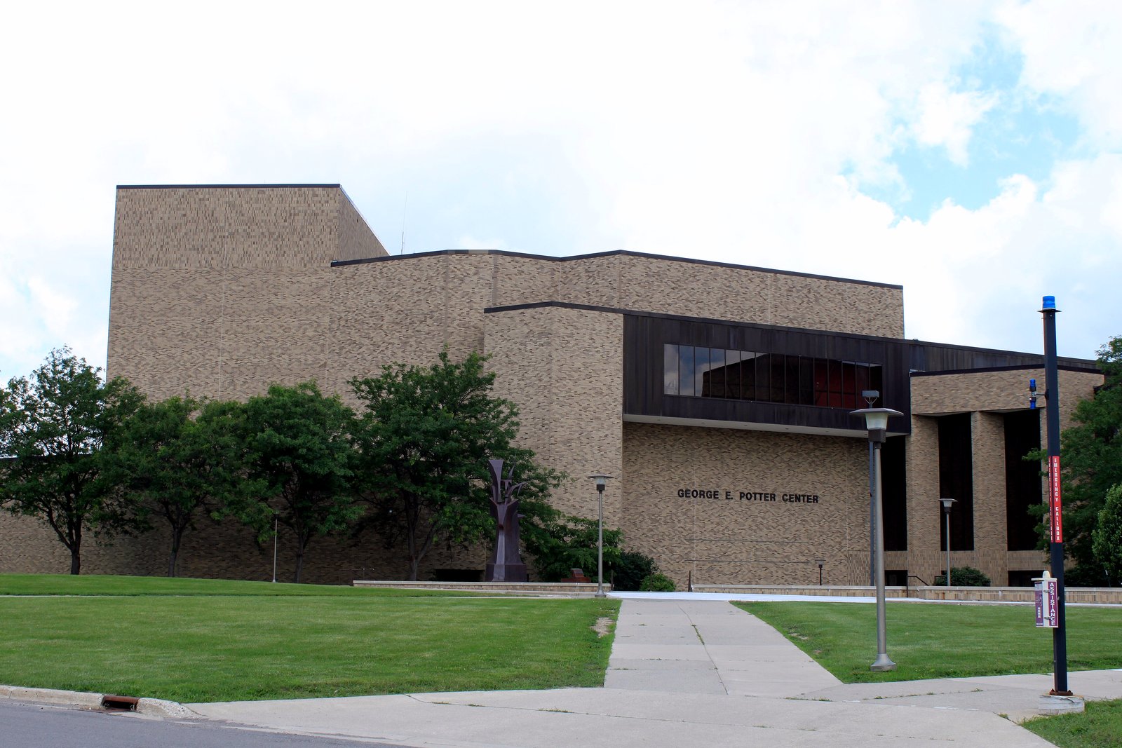 The tan brick George E. Potter Center at Jackson College, a low modern concert building with a glass entrance and trees along a sidewalk.