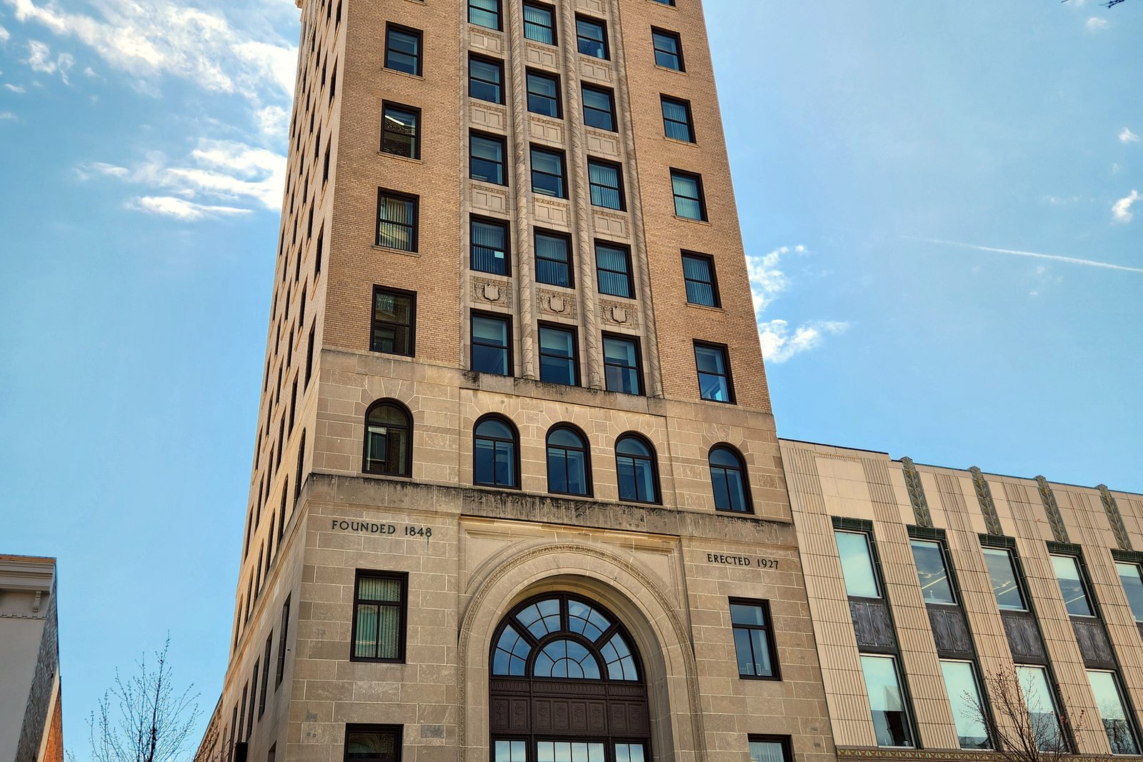 A tall tan stone office tower with an arched entrance rises against a blue sky in downtown Jackson.