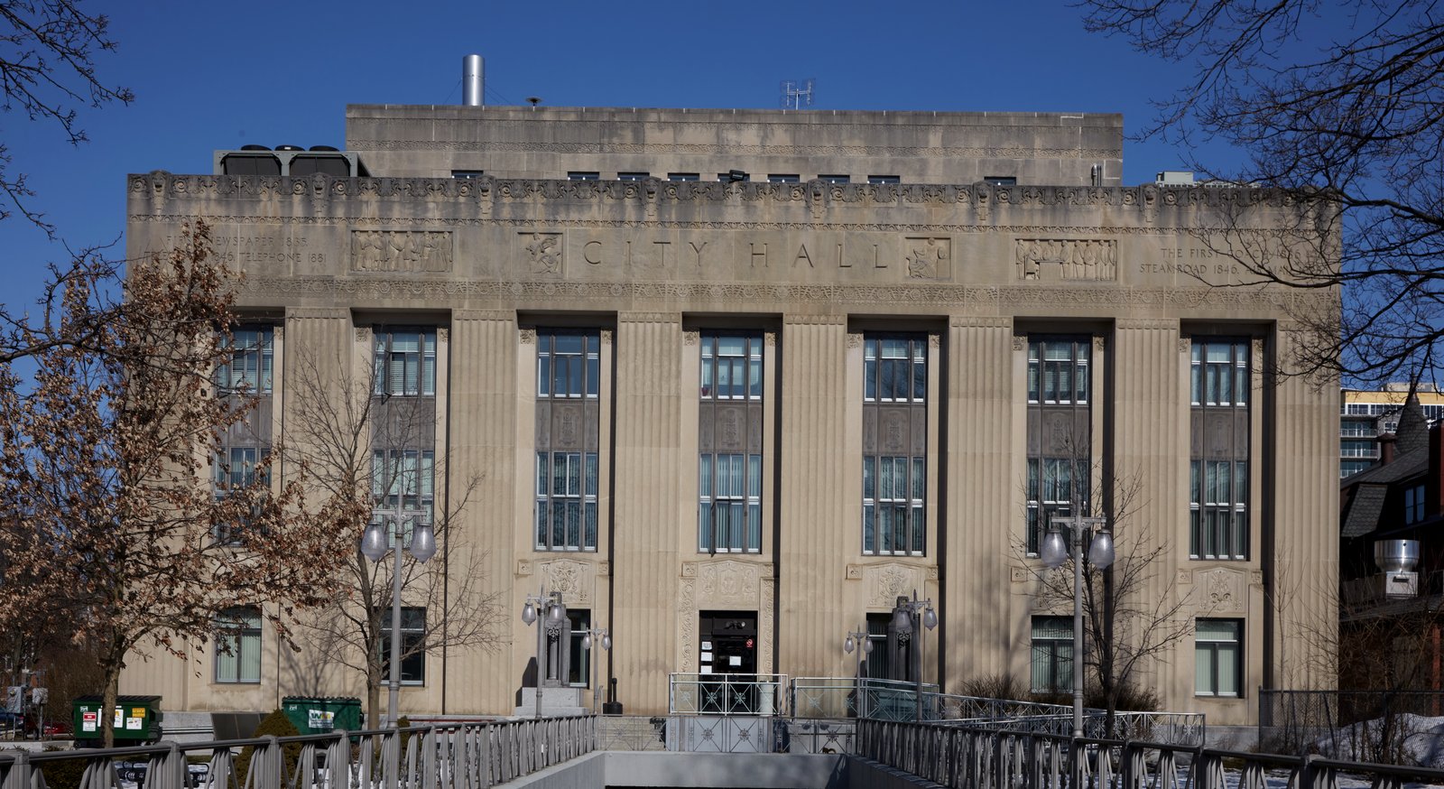 Kalamazoo City Hall, a pale Art Deco building with tall vertical windows and CITY HALL carved above them, under a blue sky.