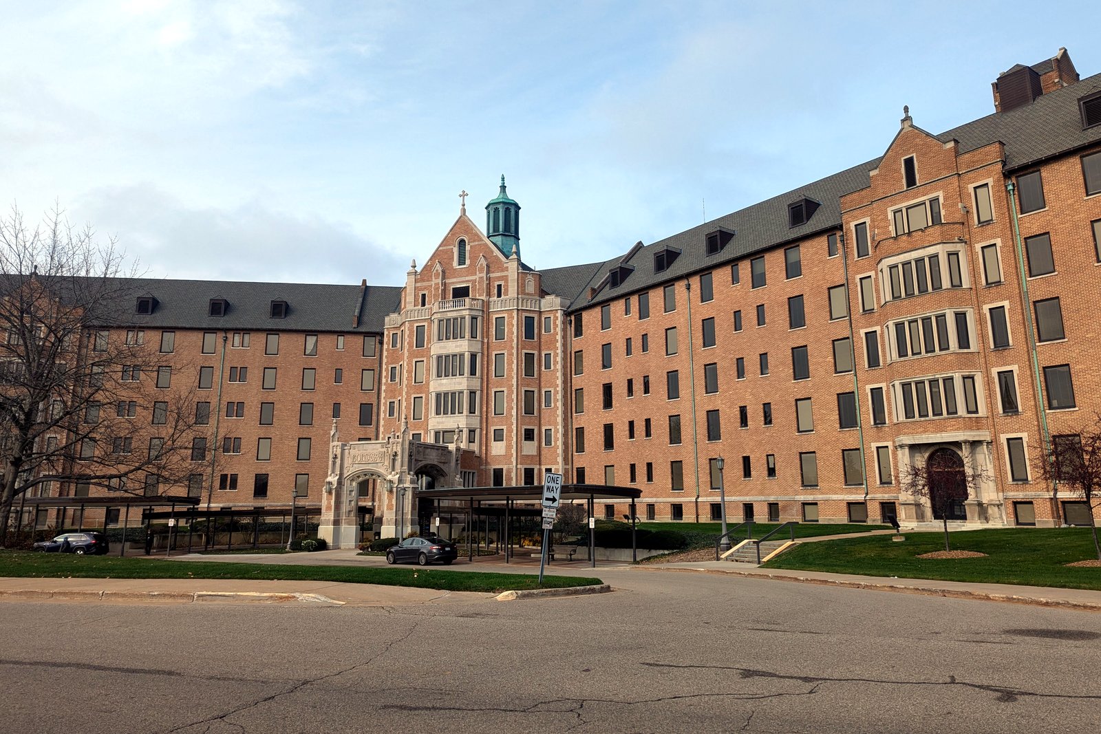 A large multistory brick hospital building with a central tower over its entrance, seen across a driveway.