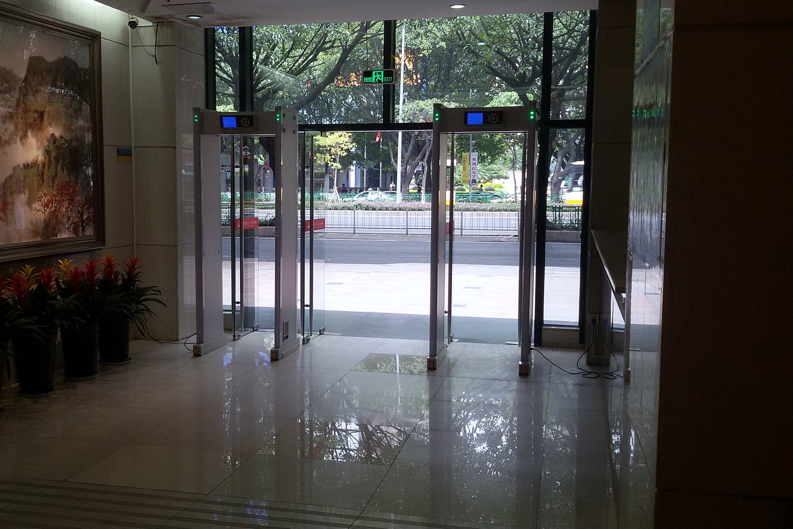 A row of walk-through security gates at the glass entrance of an office lobby with a polished floor.