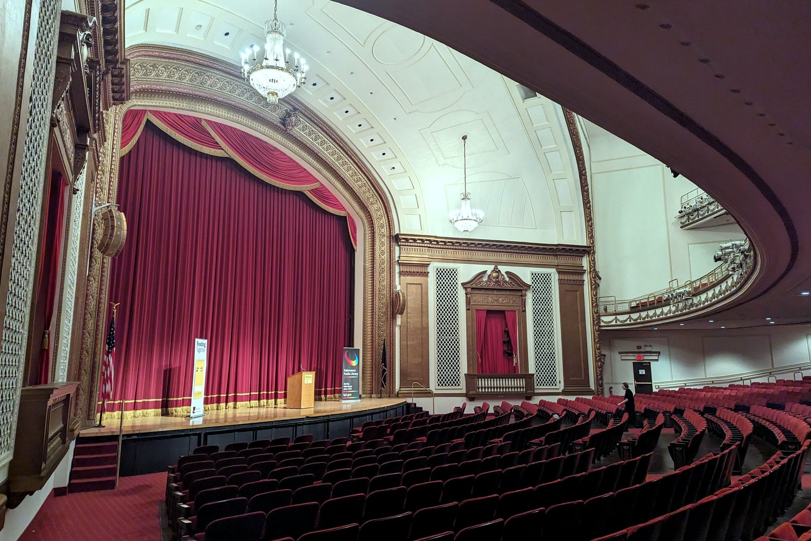 Rows of red seats facing a stage with a red velvet curtain and gilded arch inside Chenery Auditorium in Kalamazoo.
