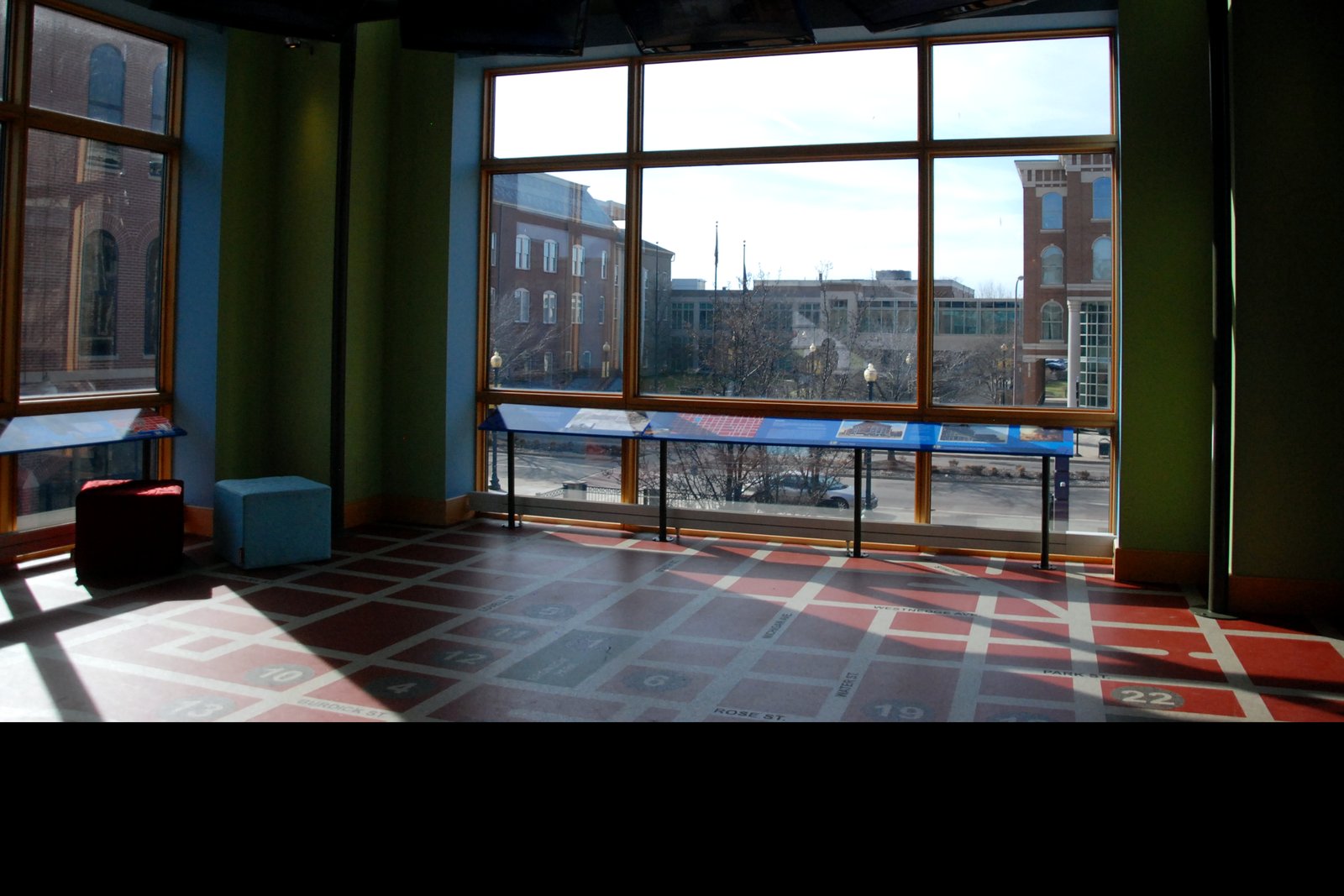 A sunlit second-floor gallery at the Kalamazoo Valley Museum, with tall windows looking out on downtown Kalamazoo and a patterned floor.