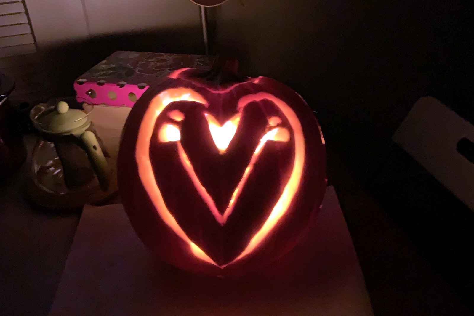 A carved pumpkin glowing orange from a candle inside, set on a table in a dim room.