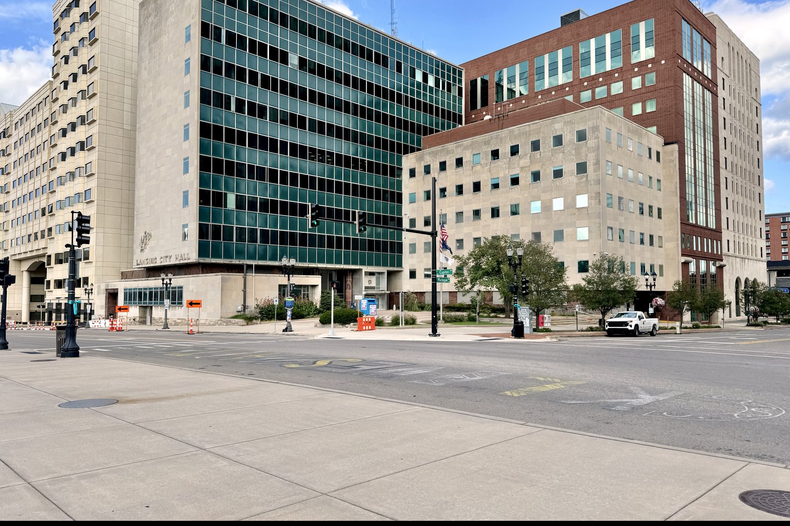 A ten-story office building with a glass curtain wall and green panels next to a six-story limestone wing at a downtown street corner, with traffic signals and an empty crosswalk in front.