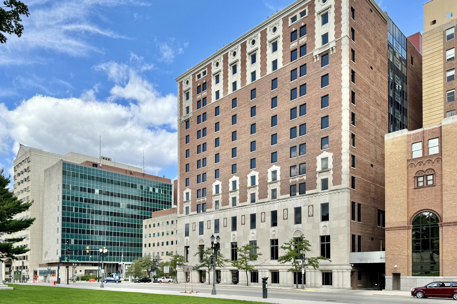 A tall modern office tower with horizontal bands of windows beside a lower brick building under a partly cloudy sky.