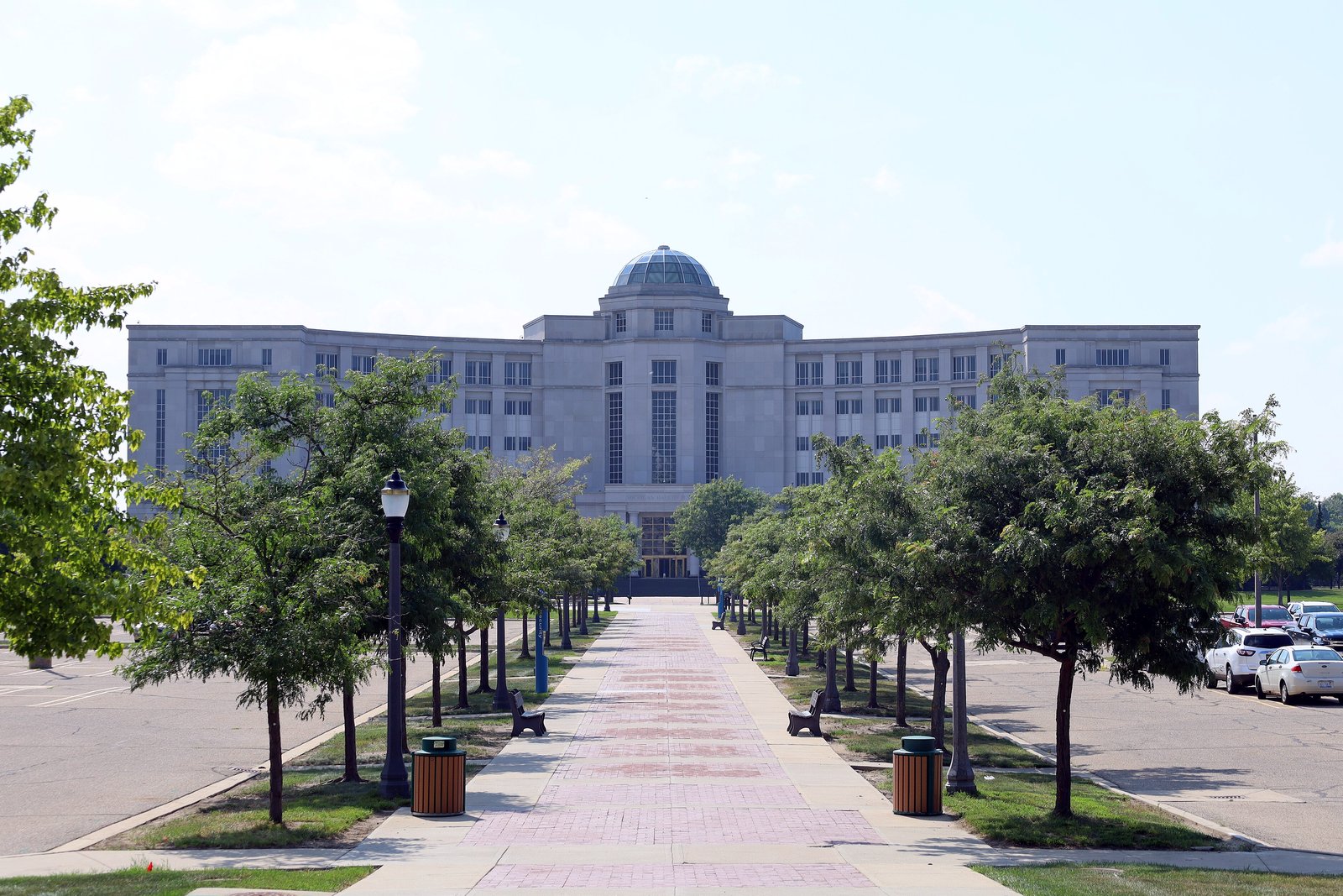 The Michigan Hall of Justice in Lansing, a long white stone building with a central dome, seen at the end of a tree-lined walkway.