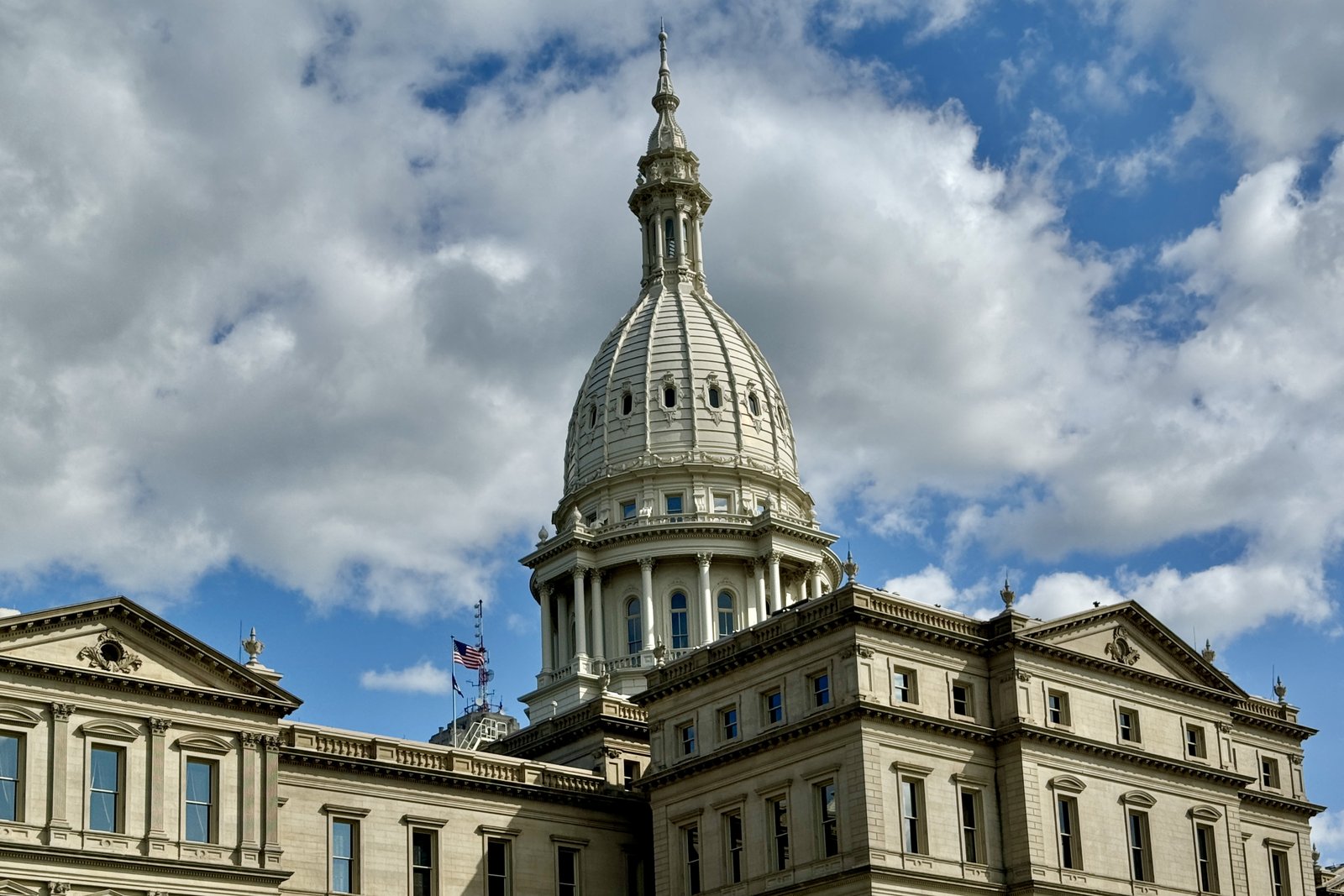 The white dome of the Michigan State Capitol rising above the building’s classical facade against a blue sky with scattered clouds.
