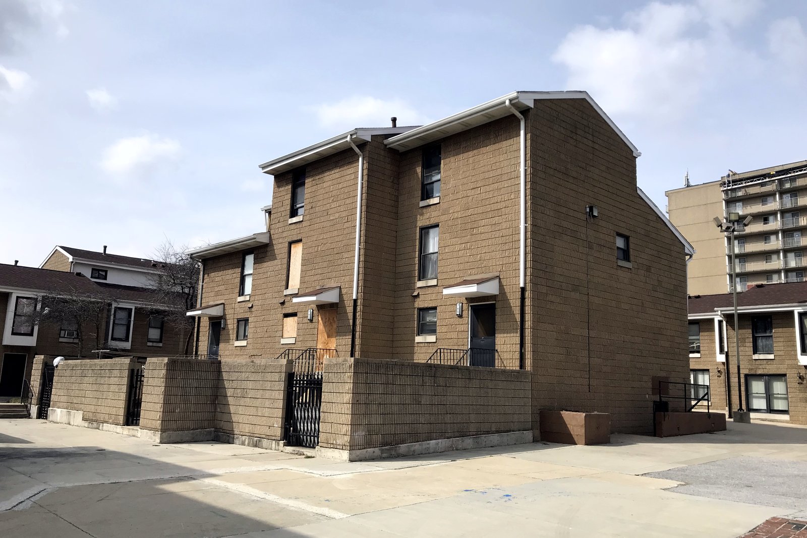 Vacant two- and three-story brick townhouse units with boarded windows around an empty paved courtyard.