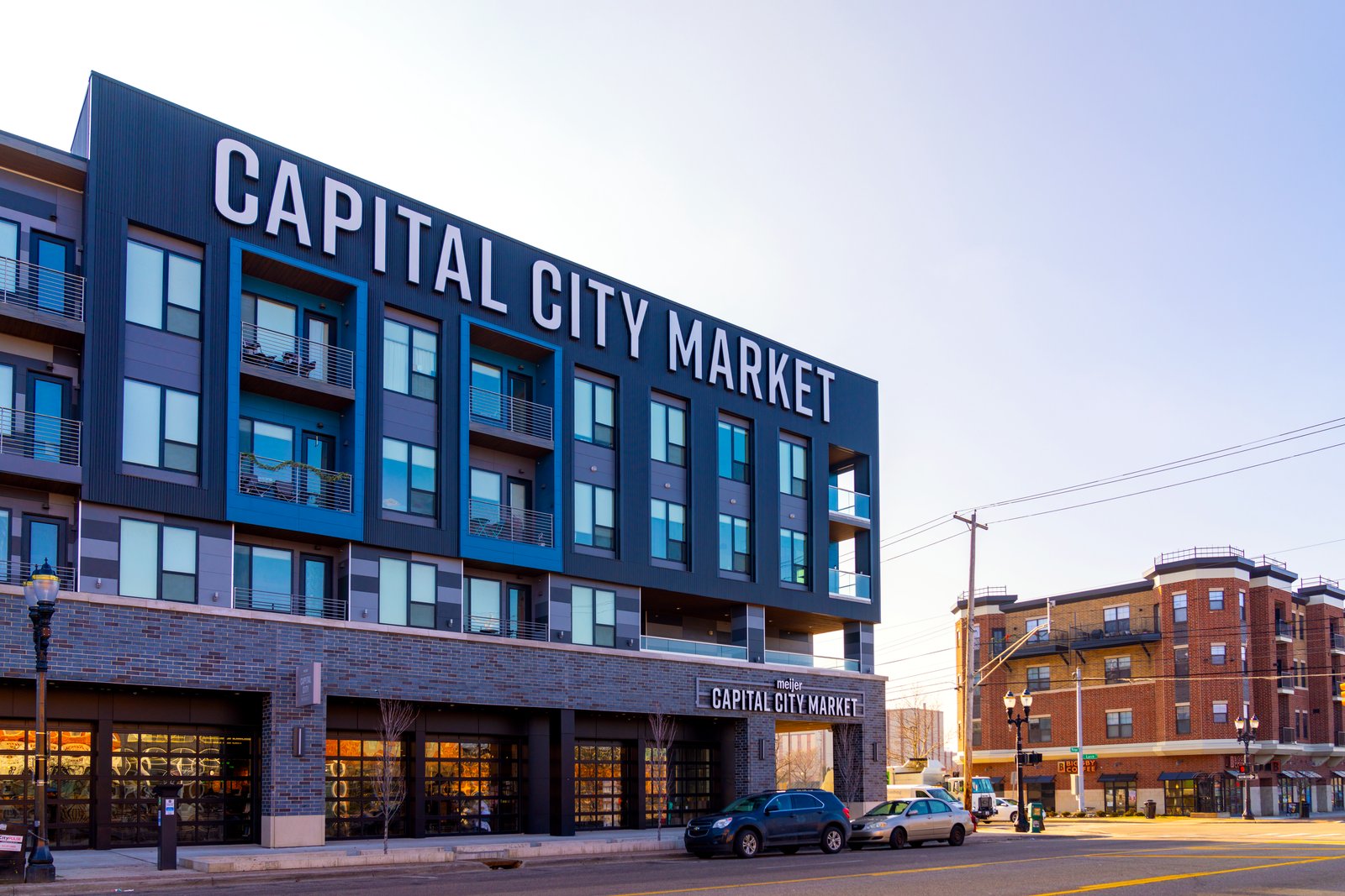 A four-story building with a large Capital City Market sign on its roof line and storefronts at street level, on a sunny day.