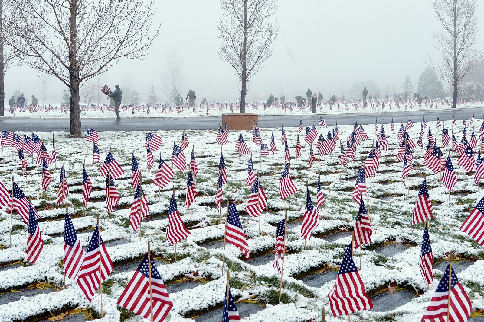 Rows of small American flags planted beside snow-dusted veterans’ grave markers in a cemetery.