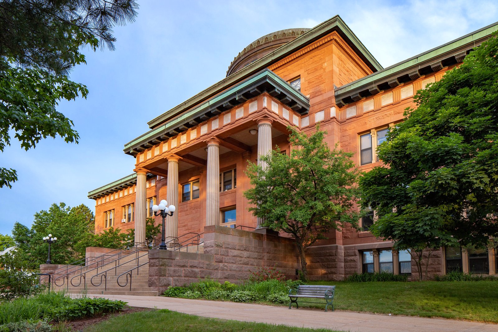 The Marquette County Courthouse, a domed sandstone building with columns, under a blue sky in Marquette, Michigan.