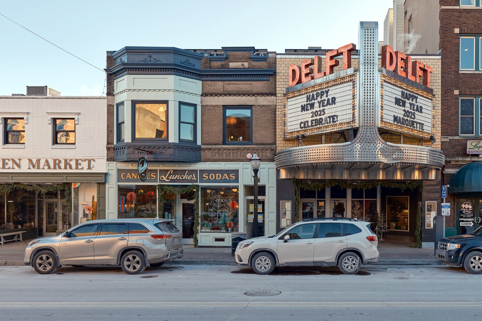 Two- and three-story brick storefronts with signs and parked cars along West Washington Street in downtown Marquette on a winter day.