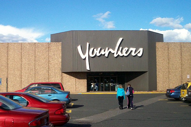 Shoppers walk across a parking lot toward the gray entrance of a Younkers department store at a mall.
