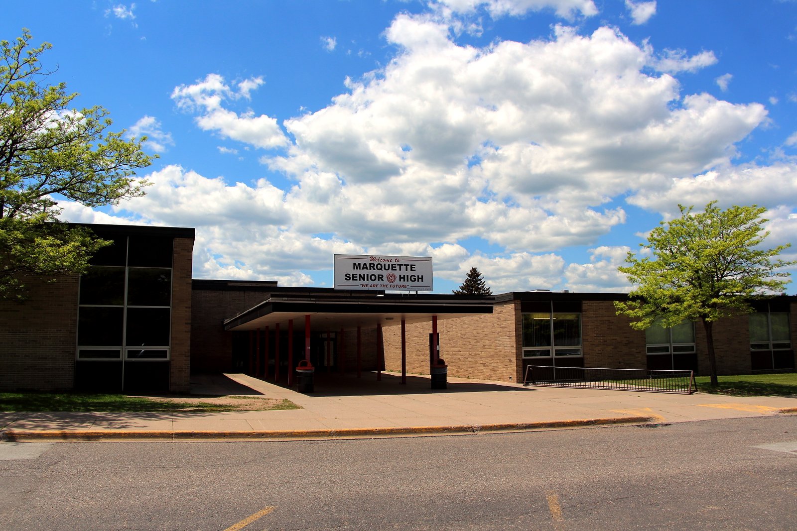 The long, low brick front of Marquette Senior High School with a lawn and trees under a blue sky.