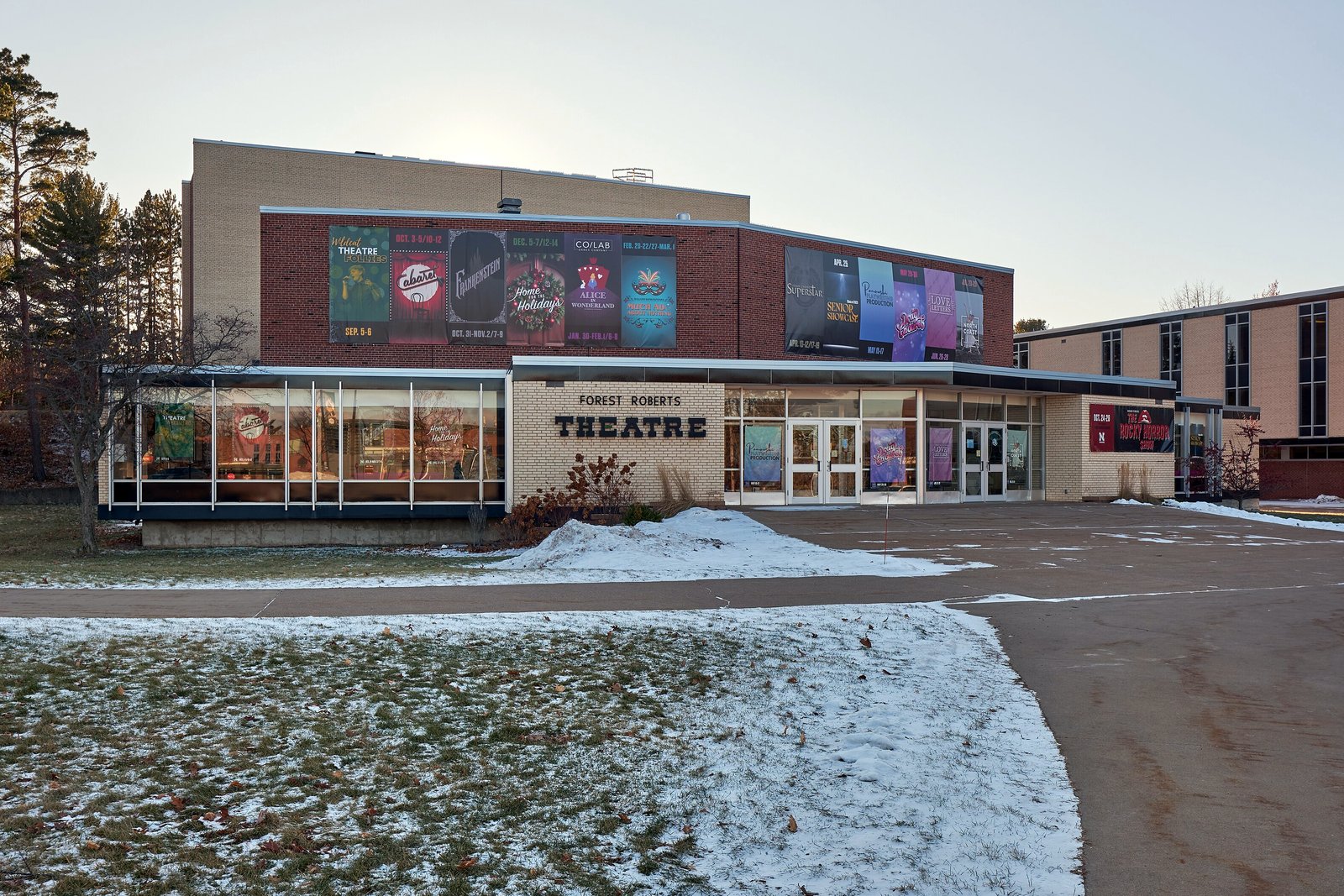 The glass and brick main entrance of the Forest Roberts Theatre at Northern Michigan University, with snow on the ground.